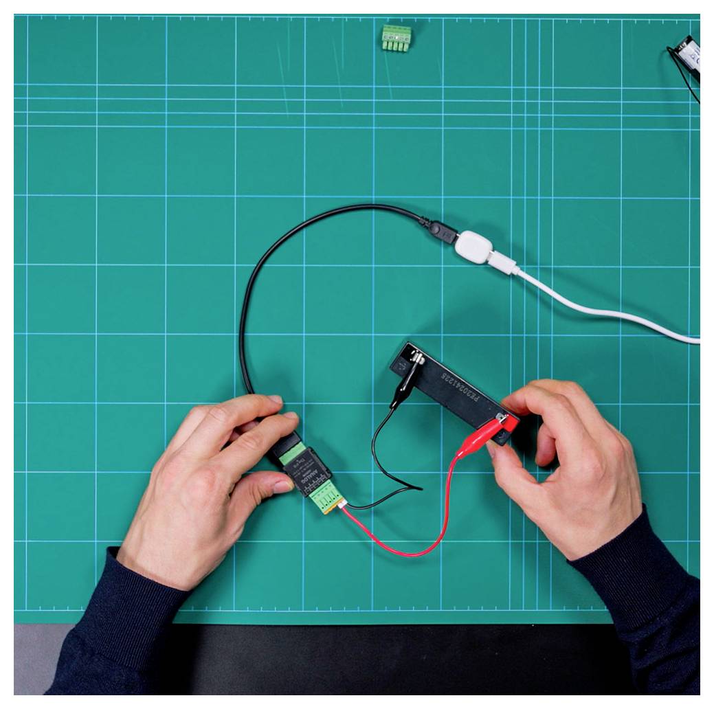 'Handen die draden aansluiten op elektronische componenten op een blauwe mat met rasterpatroon, waardoor het montageproces van een elektronisch circuit wordt aangetoond.'
