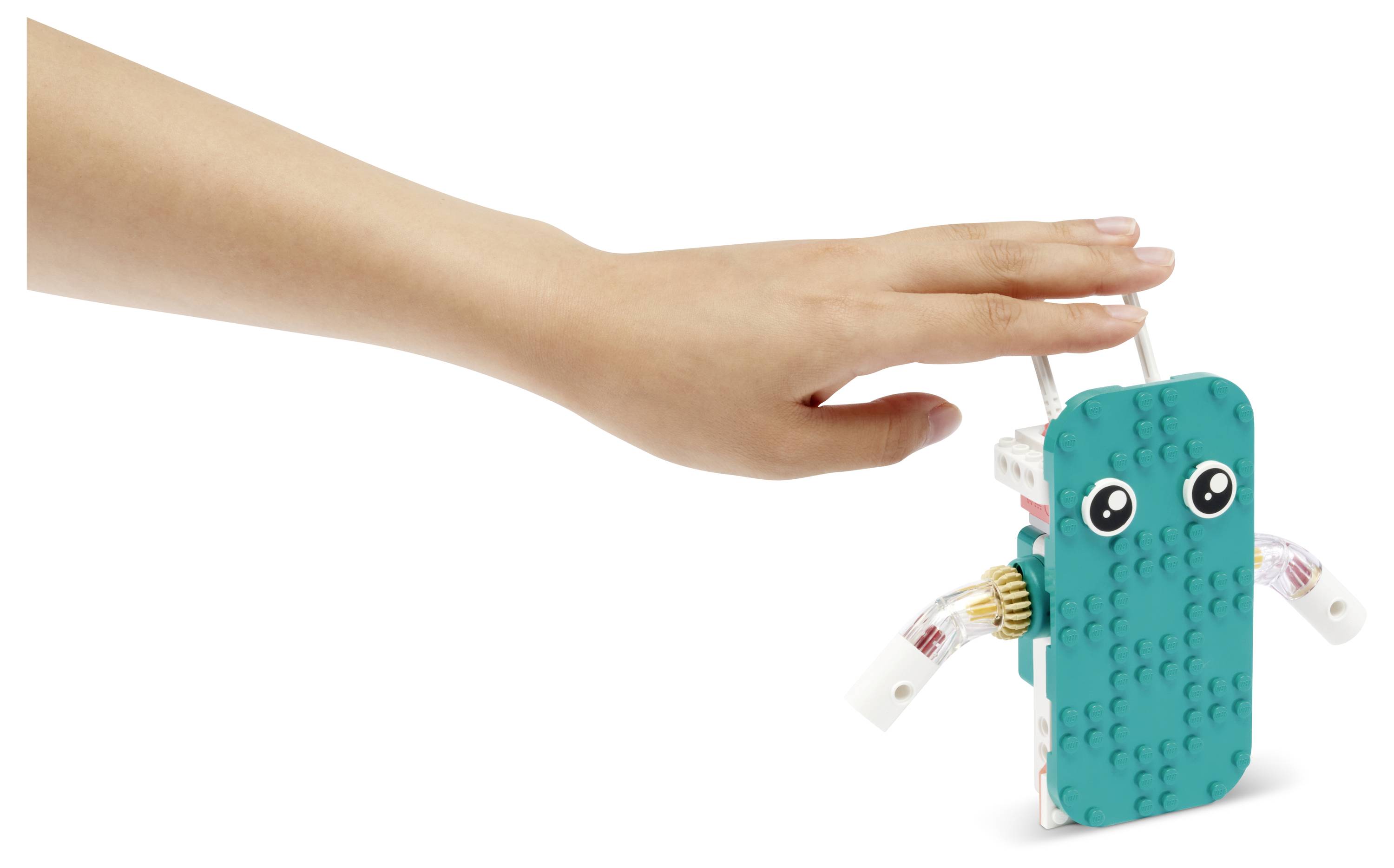 Een hand steekt uit om een klein robotje met blauwe bekleding en wiegende ogen aan te raken, dat lijkt op een speelgoed, tegen een witte achtergrond.