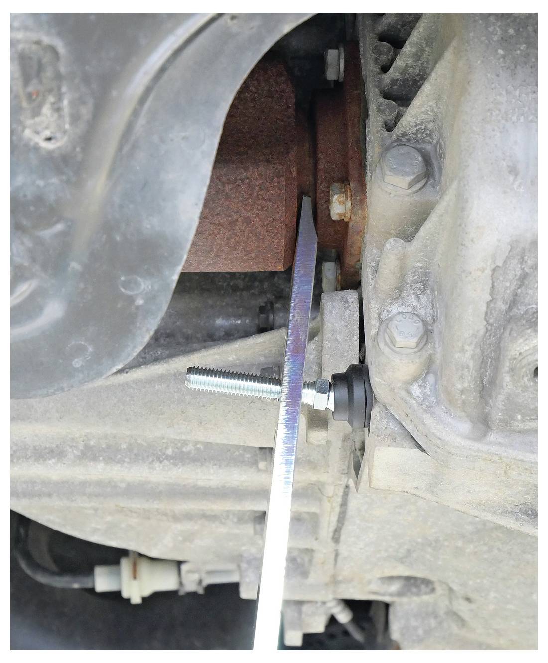 Gereedschap dat kracht uitoefent op een verroest autodeel voor verwijdering, demonstrerend mechanische hefboomwerking in auto-reparatie.