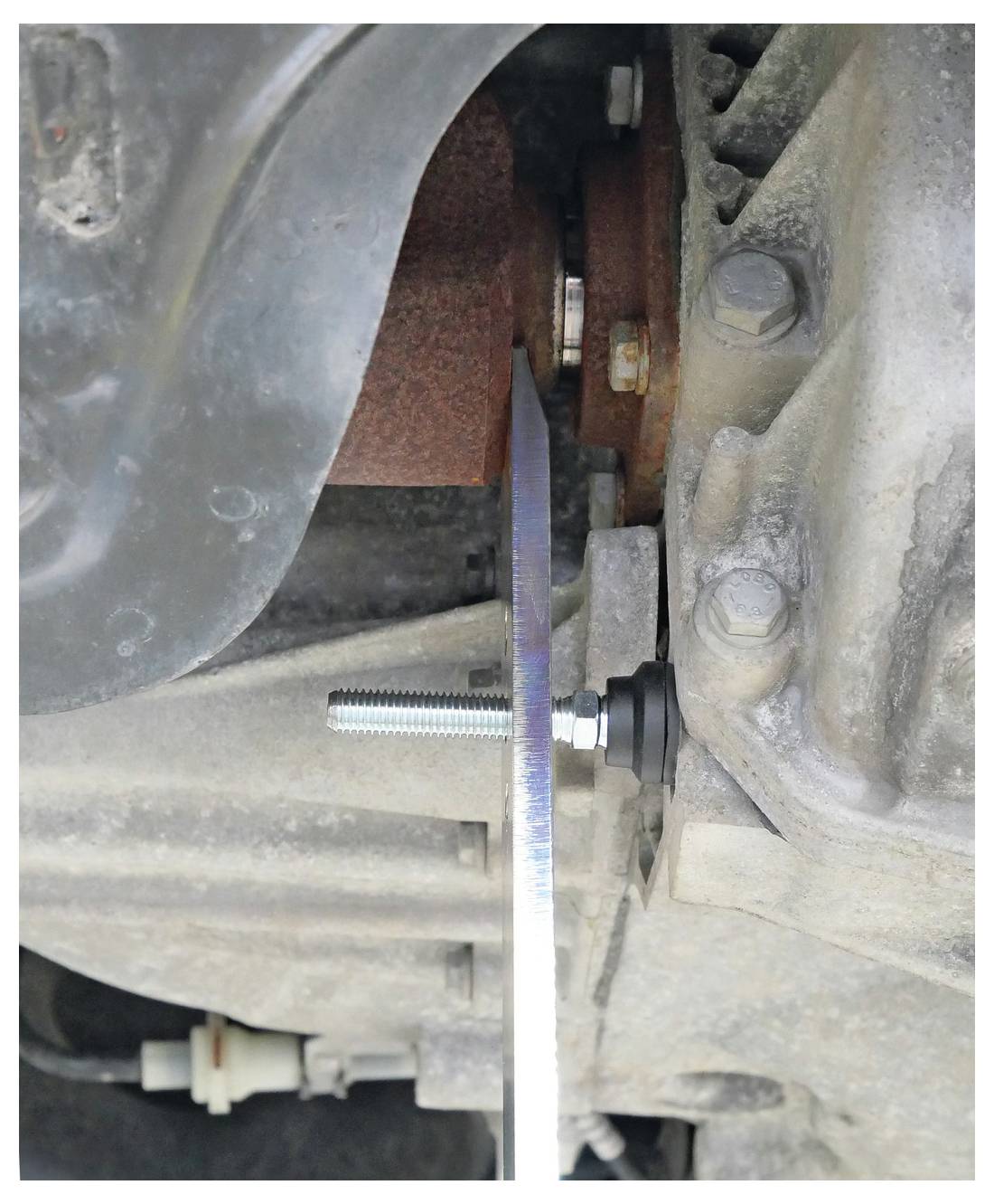 'Close-up van een roestige auto-uitlaat met een metalen zaagblad erin geplaatst voor het snijden. Bouten en mechanische onderdelen zijn zichtbaar, wat wijst op reparatiewerkzaamheden.'