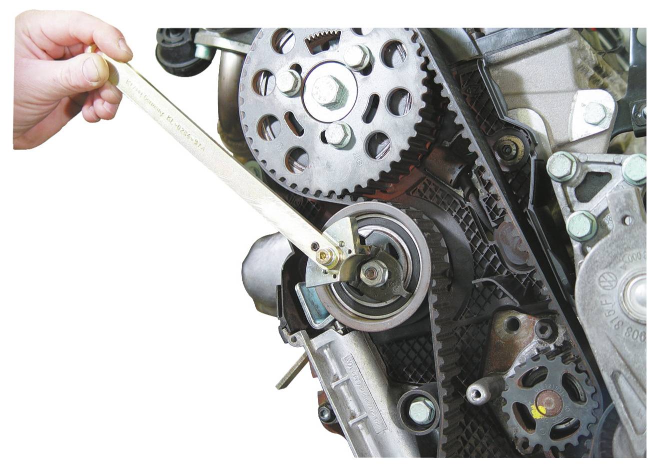 Een hand stelt de spanning van een autoriemschijf bij met behulp van een sleutel. De afbeelding benadrukt de positie van de riem en het spanmechanisme.