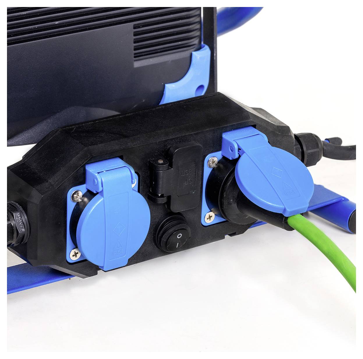 Een apparaat met meerdere blauwe elektrische stopcontacten, één stopcontact heeft een groene kabel ingestoken. De achtergrond toont een deel van de zwarte en blauwe behuizing.