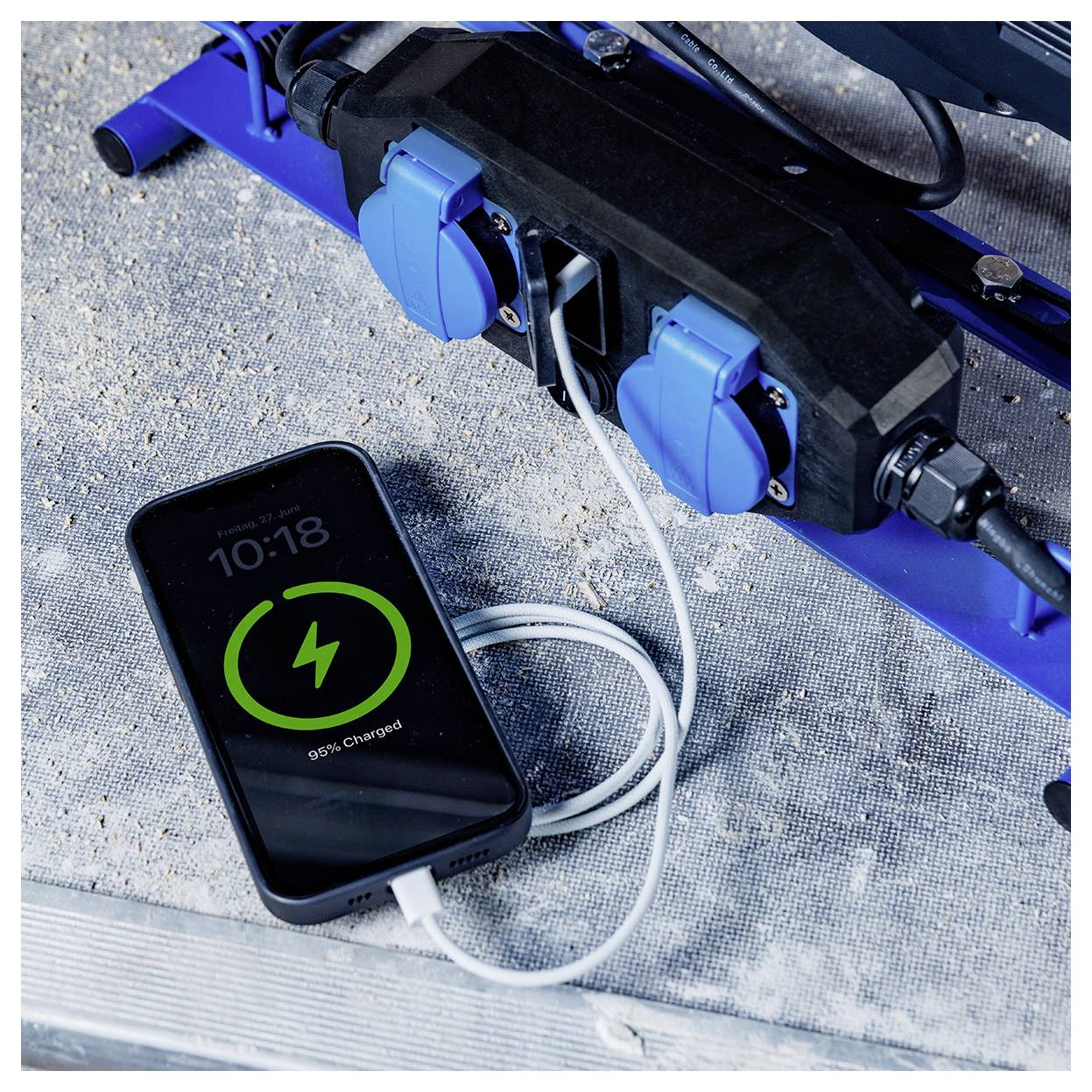 'Een smartphone met 95% batterij aangesloten op een stroomverdeler met meerdere contactdozen op een metalen oppervlak.'