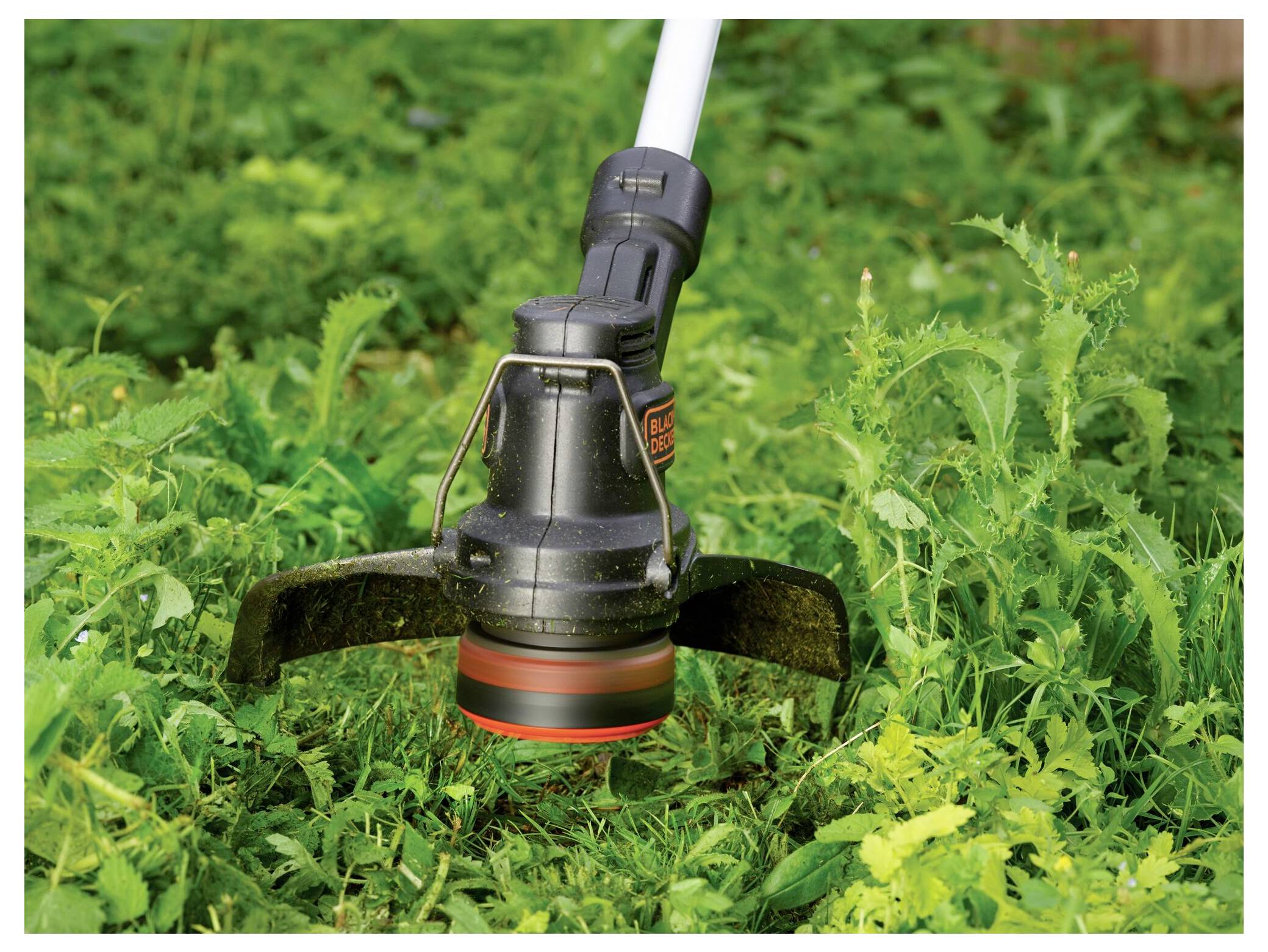 Een grassnijder snijdt door hoog gras en onkruid in een tuin heen, wat zijn effectiviteit bij gazononderhoud aantoont.
