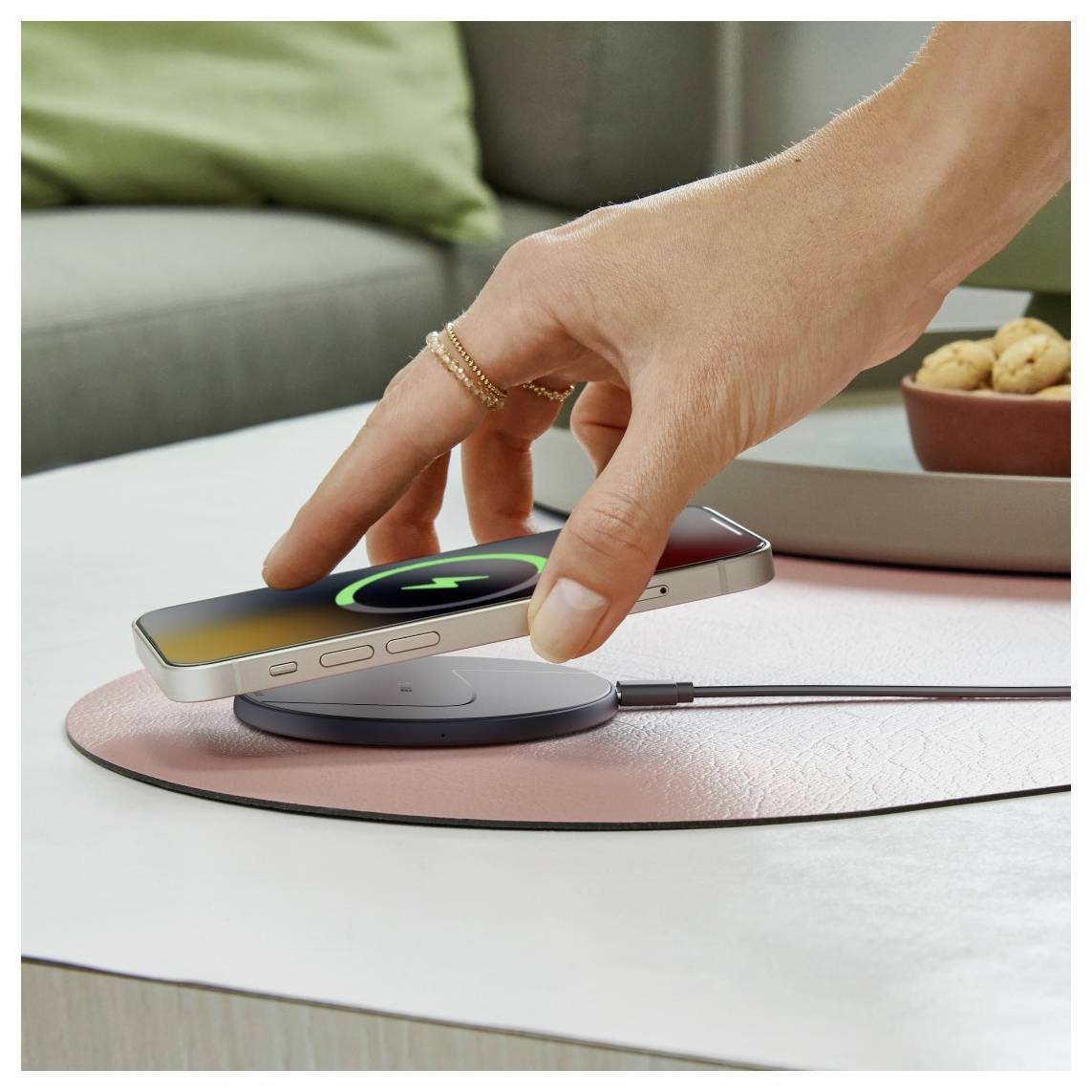 Een hand plaatst een smartphone op een draadloos laadkussen. Het scherm van de telefoon toont een laadsymbool, wat aangeeft dat deze begint op te laden.