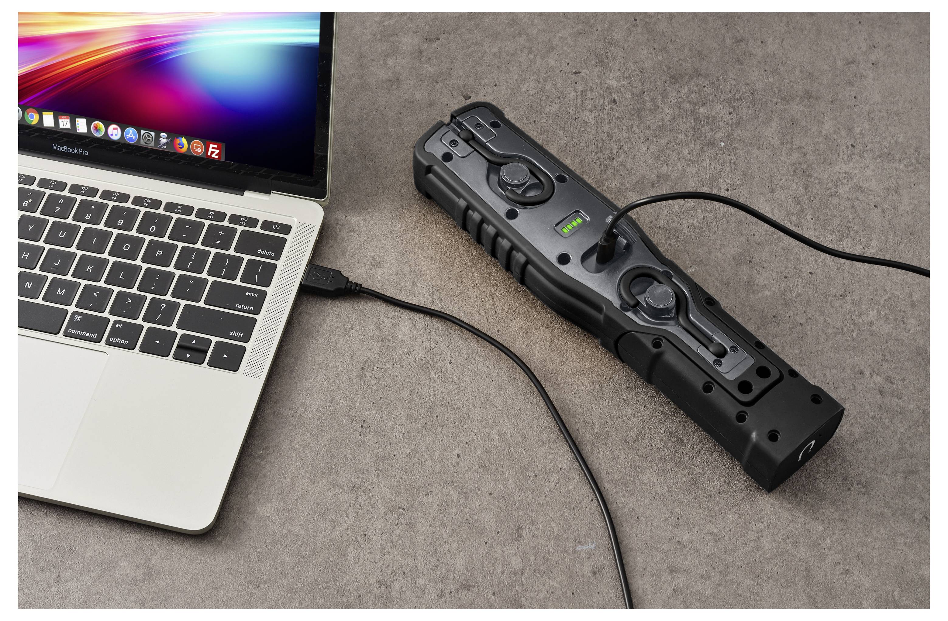Laptop verbonden via kabel met een zwart draagbaar stroomstation op een tafelblad, met het indicatielampje van de powerbank aan.