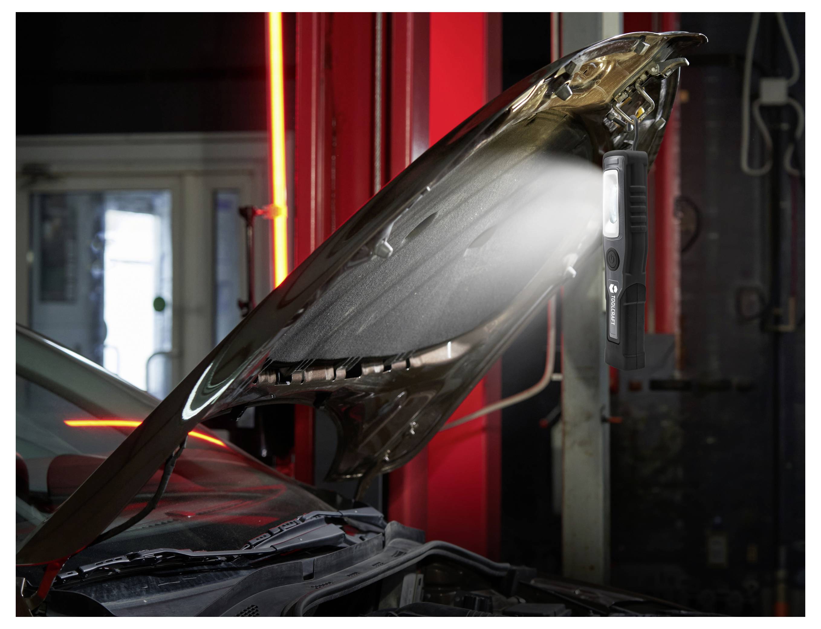 Autodak omhoog geklikt in een autowerkplaats, waardoor de motorruimte onder felle inspectielichten zichtbaar wordt.