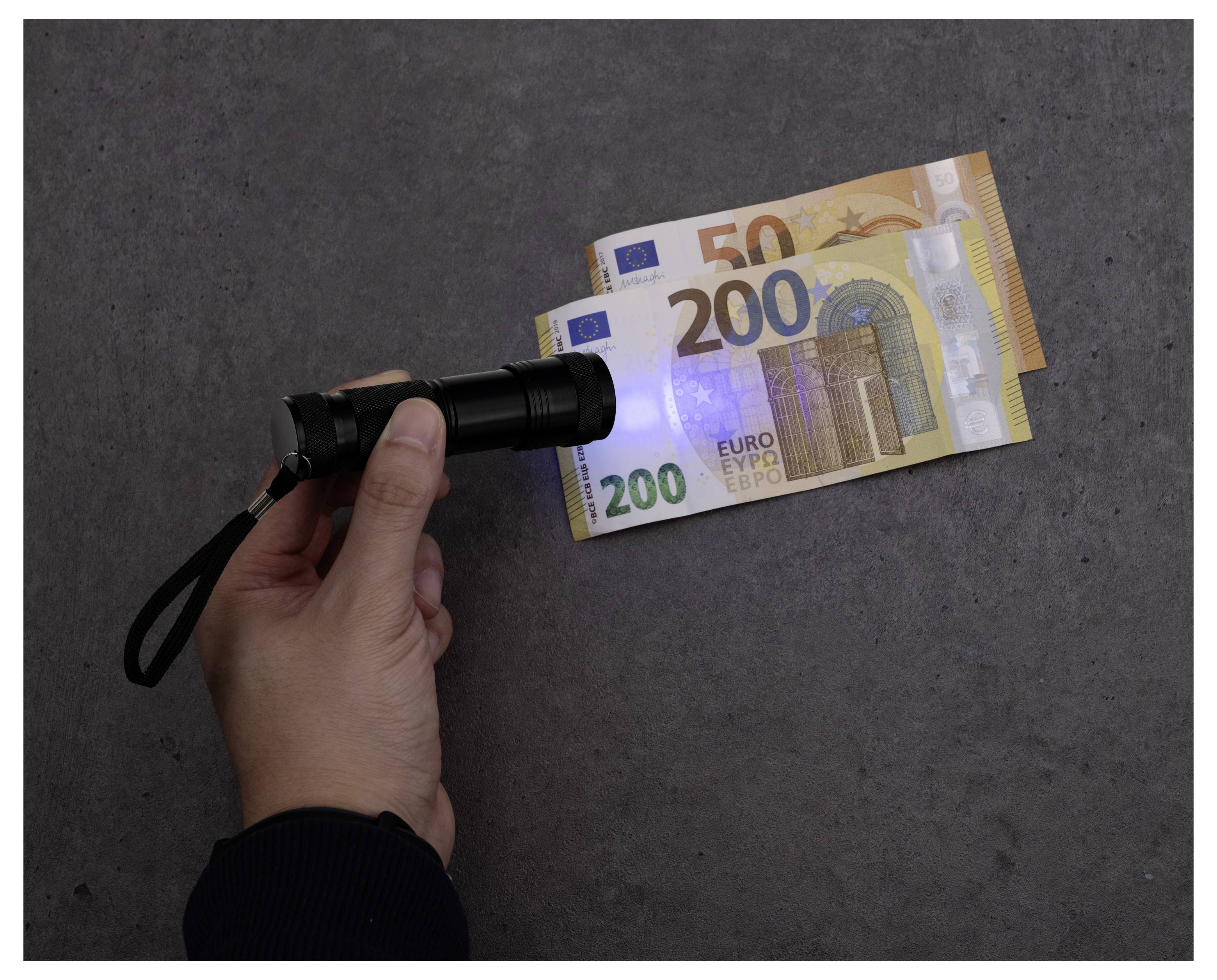 Een hand die een zaklamp vasthoudt boven 50 en 200 euro biljetten, verlicht de bankbiljetten op een donker oppervlak.