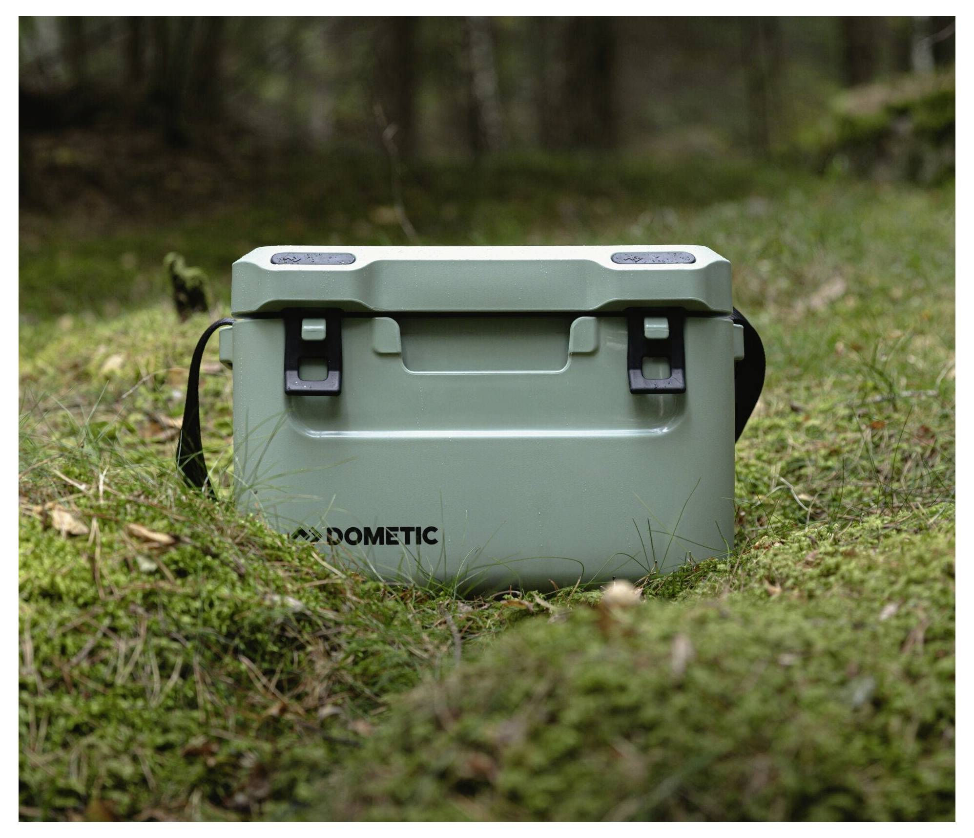 Mint-groen Dometic-koelbox zittend op gras in een bosachtige buitenomgeving.