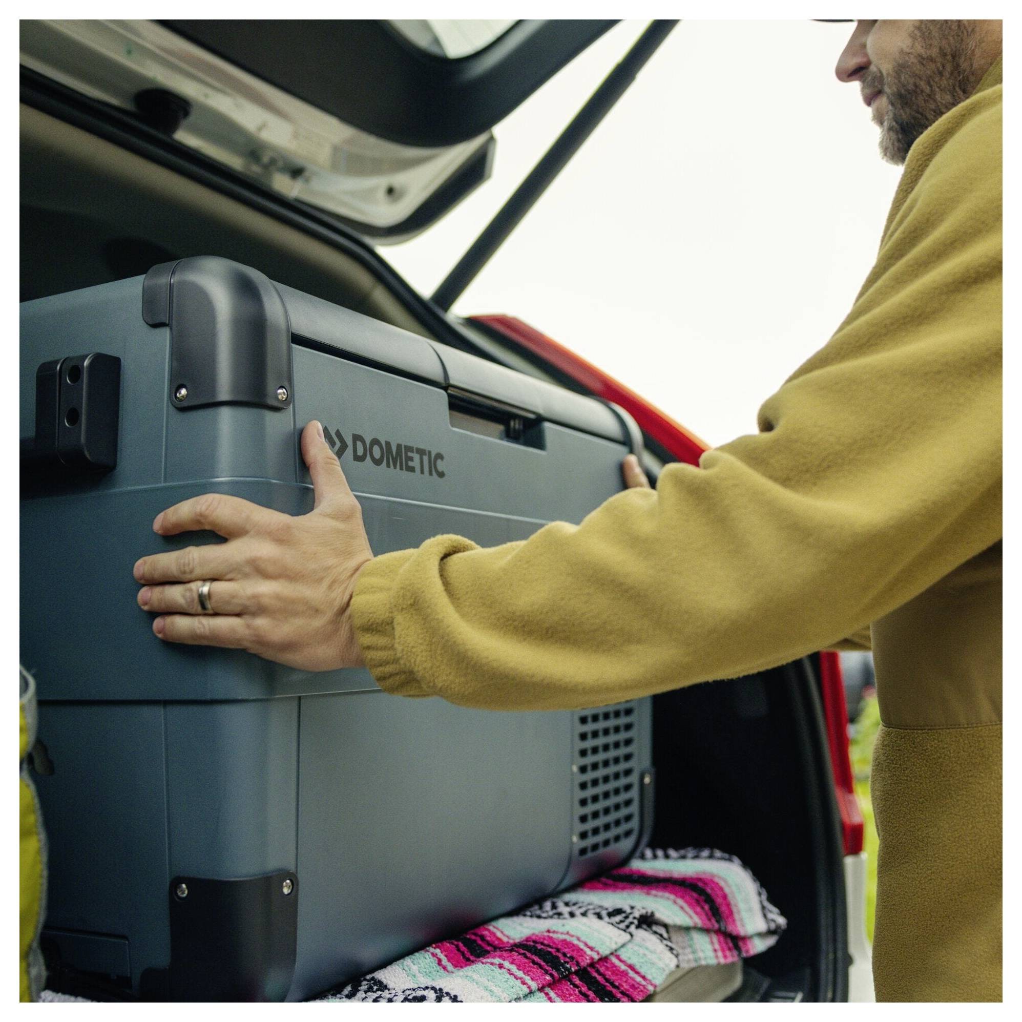 Man die een Dometic-koelbox in de open kofferbak van een auto laadt, met een deken eronder.