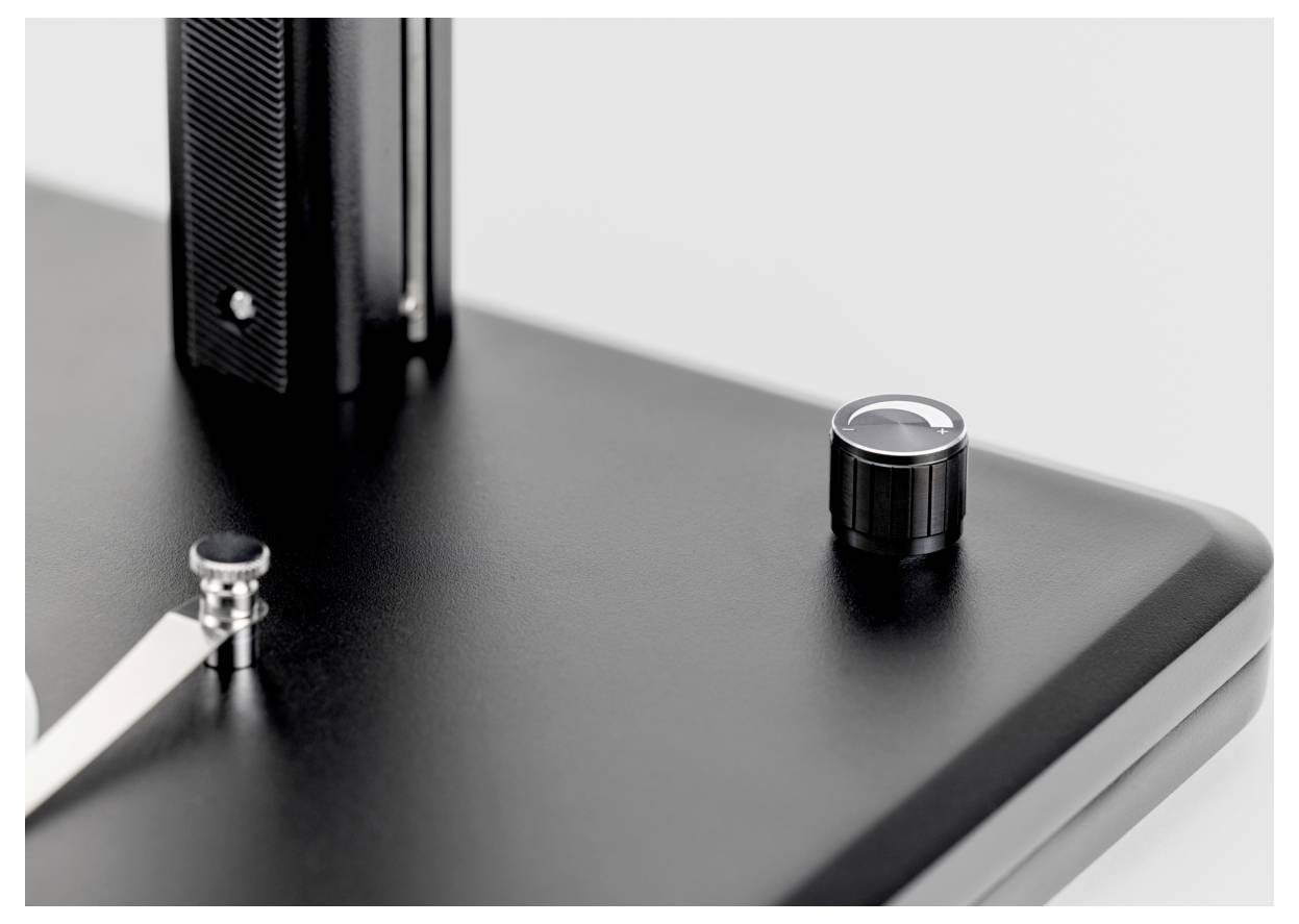 Een close-up van een gladde, zwart metalen oppervlakte met een glanzende knop en een klein voetje, die moderne industriële designelementen toont.