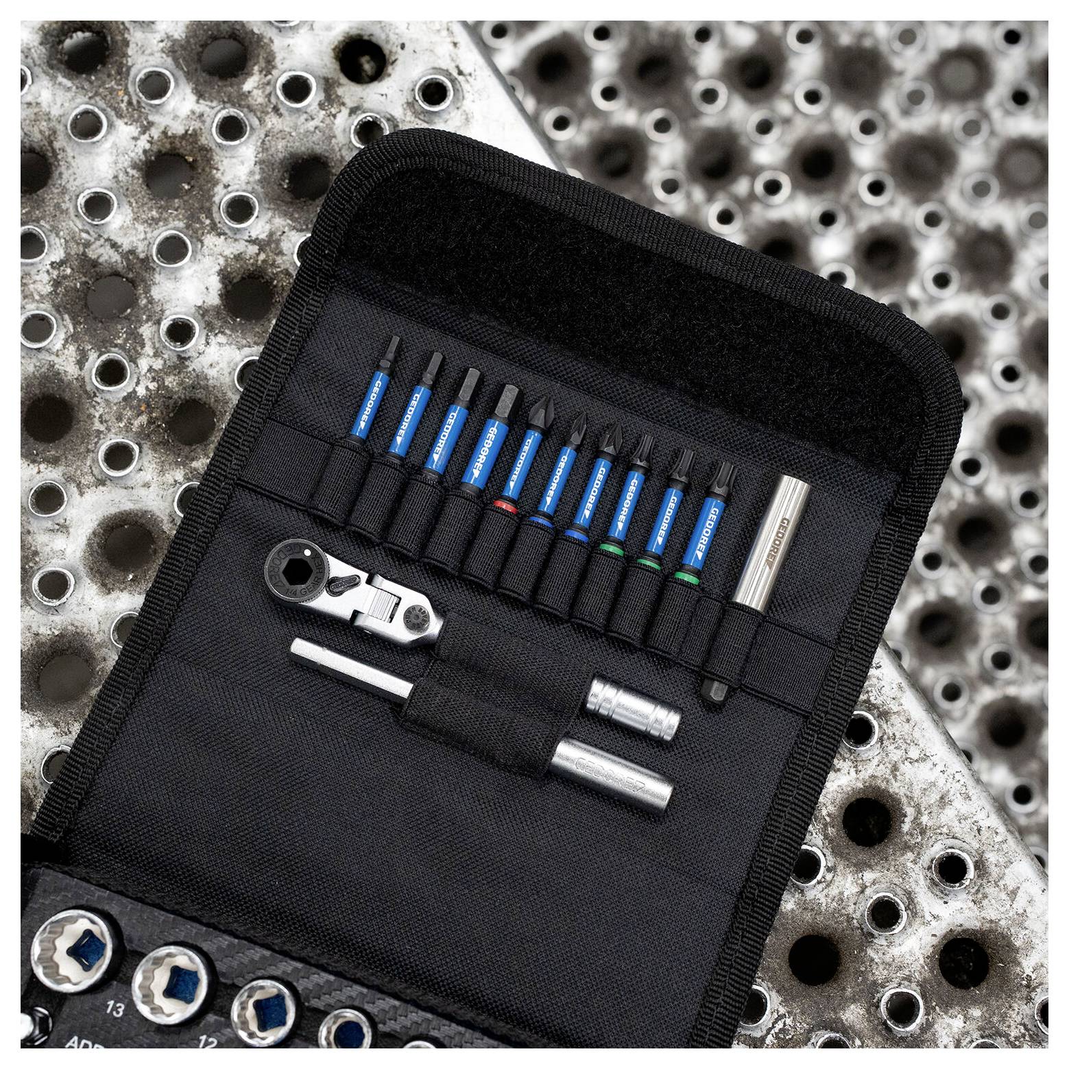 Open zwart gereedschapskoffertje met blauwe handvaten markers, een ratel, sockets en een pen op een geperforeerd metalen oppervlak.