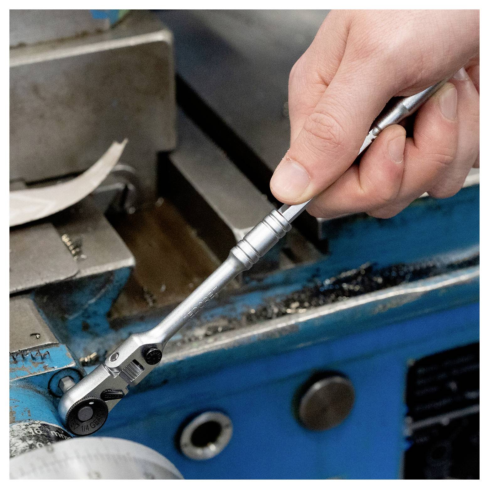 Close-up van een hand die een ratelbeugelsleutel gebruikt op een metalen machinedeel, wat duidt op mechanisch onderhoud of reparatie.