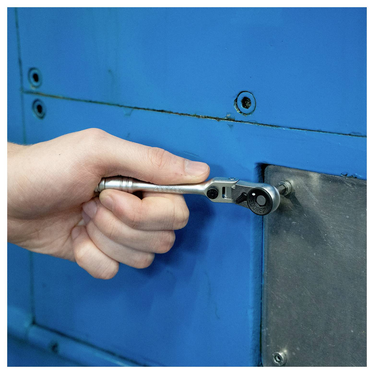 Hand die een steeksleutel gebruikt om een bout op een blauw metalen machinepaneel aan te draaien.