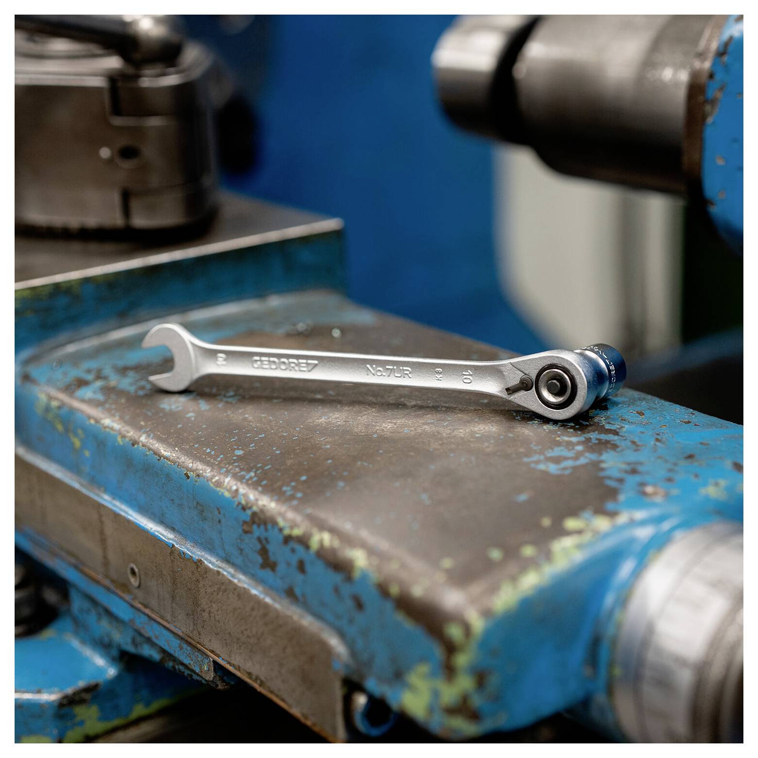 Een metalen kliktang ligt op een versleten blauwe machineoppervlak in een werkplaats.