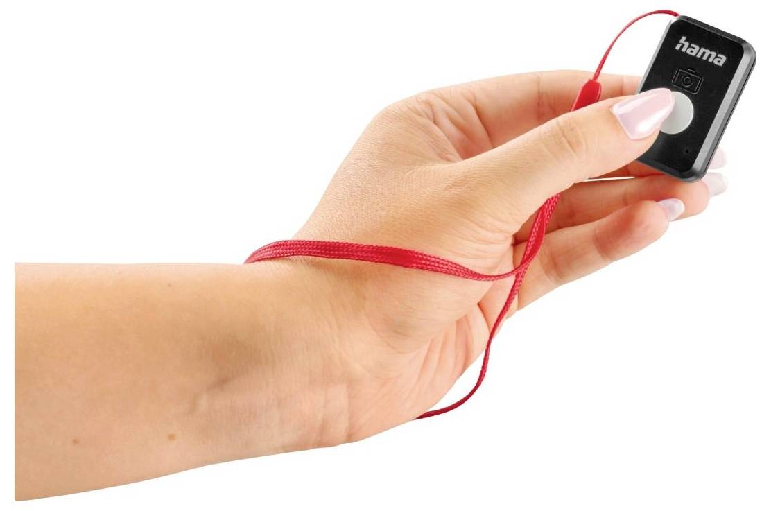 Een hand houdt een klein, vierkant zwart afstandsbediening met een rode polsband vast.