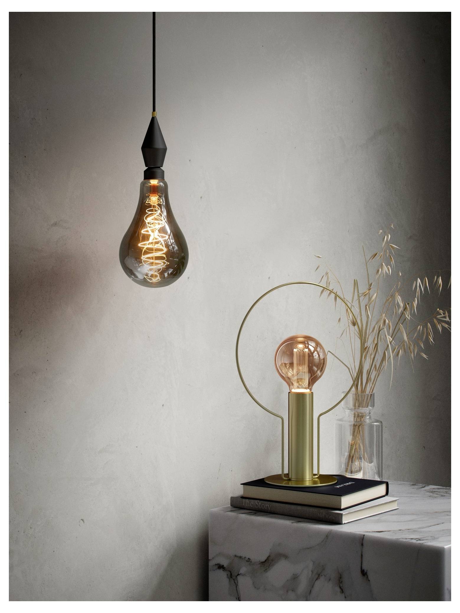 Een minimalistische omgeving met een vintage Edisonlamp die hangt, een aangestoken tafellamp naast boeken, en droogbloemen in een vaas op een marmeren oppervlak.