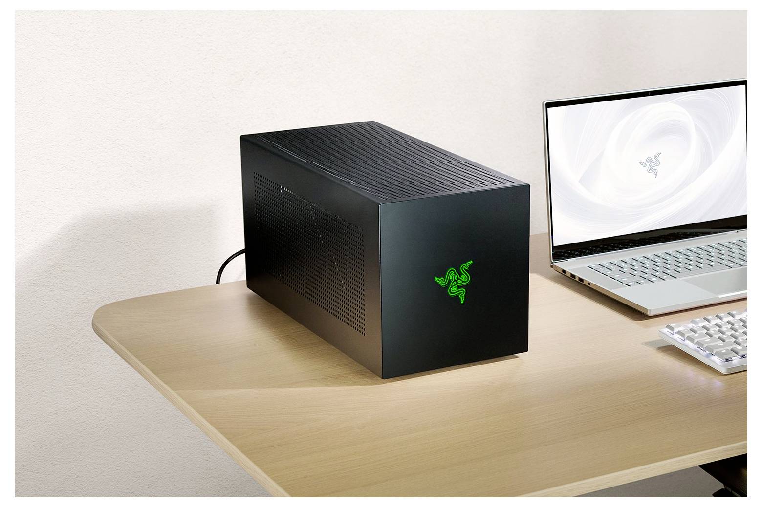 Een zwarte externe GPU-behuizing met een groen logo staat op een houten bureau naast een open zilveren laptop die een soortgelijk logo toont.
