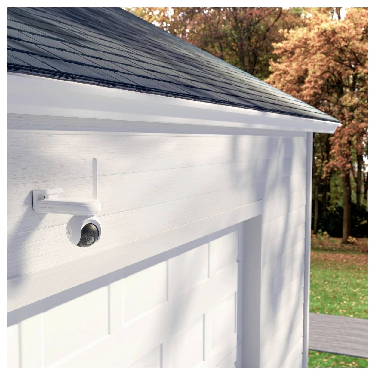 Een witte garage met een beveiligingscamera gemonteerd op de hoek, omgeven door herfstbomen.