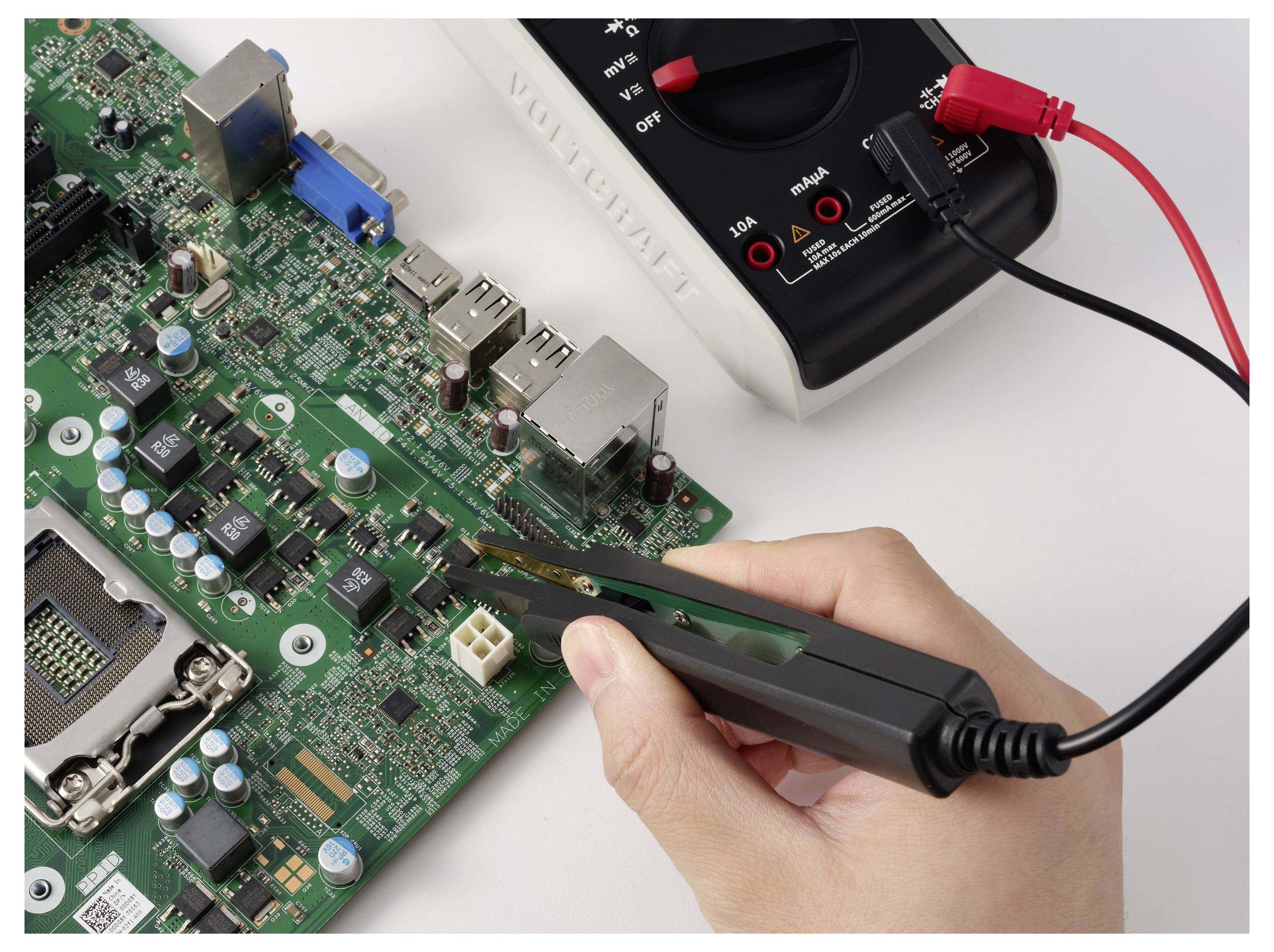Hand die een pincet vasthoudt onderzoekt een printplaat terwijl een multimeter met rode en zwarte meetdraden de componenten test.
