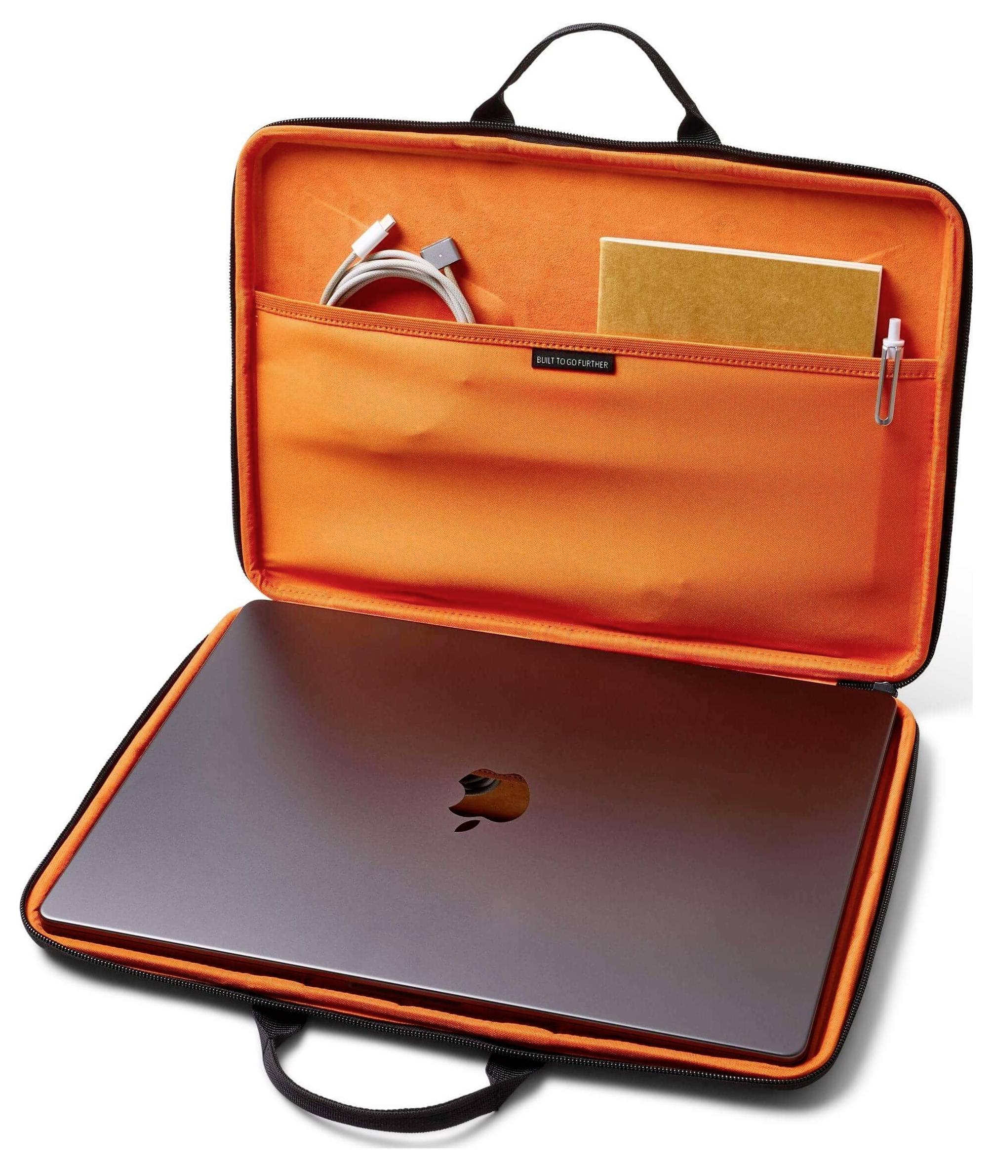 Een open oranje laptoptas onthult een dichte laptop, een opgerold kabel, een notitieboek en een pen, allemaal netjes georganiseerd in vakken.