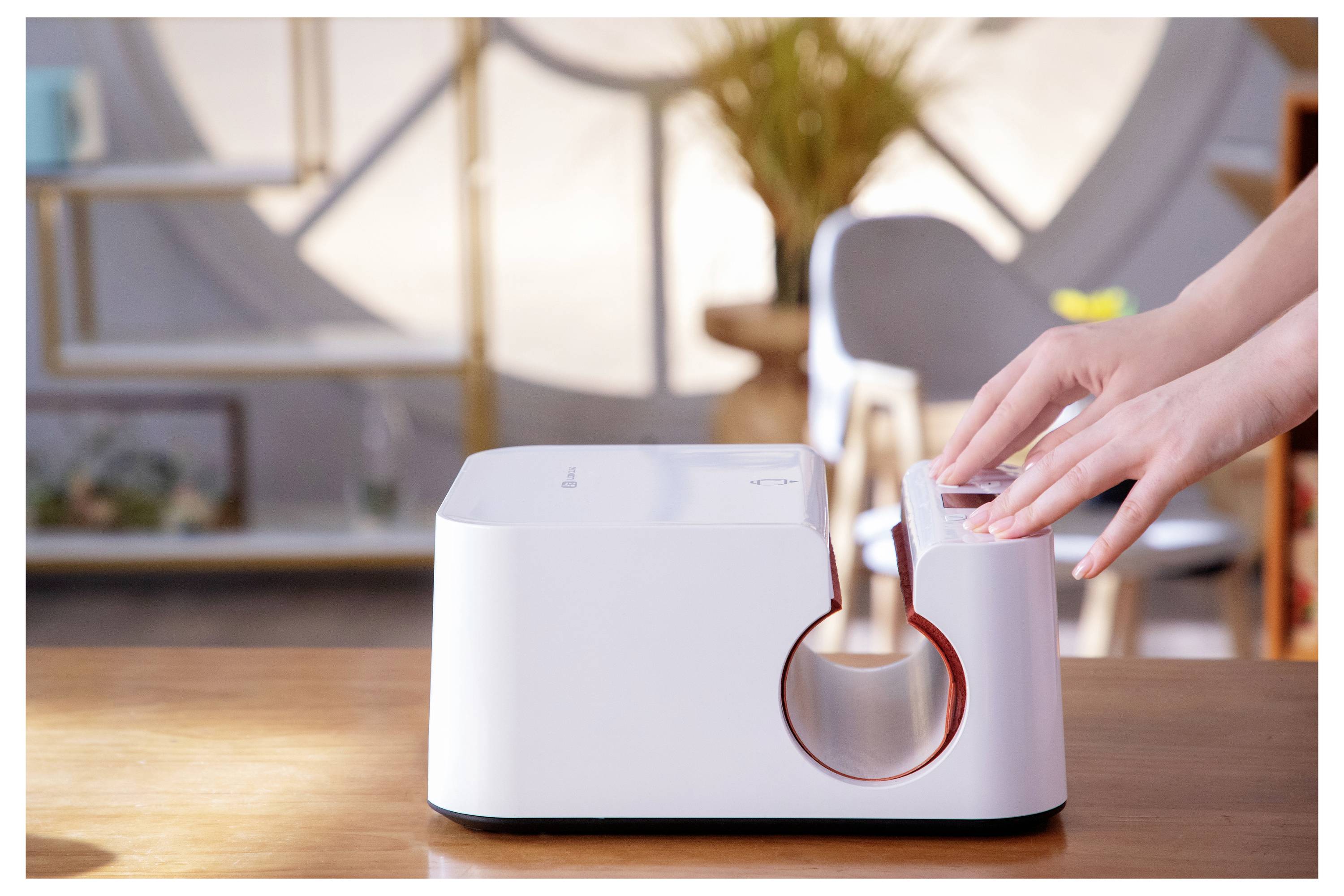 Een persoon die een identiteitsbewijs laminaatverwijdert met behulp van een witte machine op een houten tafel in een helder verlichte kamer met kasten en een stoel op de achtergrond.