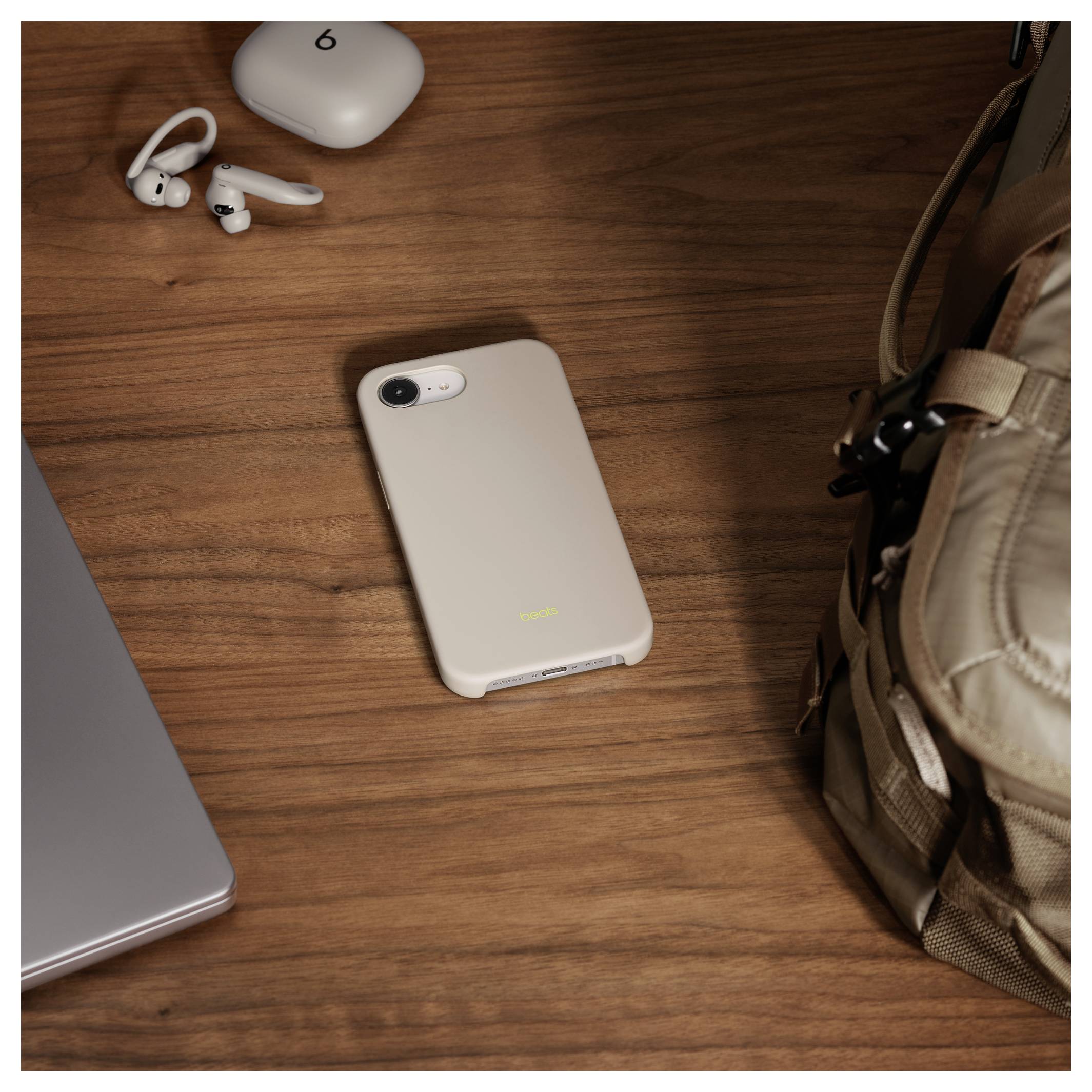 Smartphone in een beige hoesje op een houten bureau met rugzak, laptop, oordopjes, wat op een reis- of werkopstelling suggereert.
