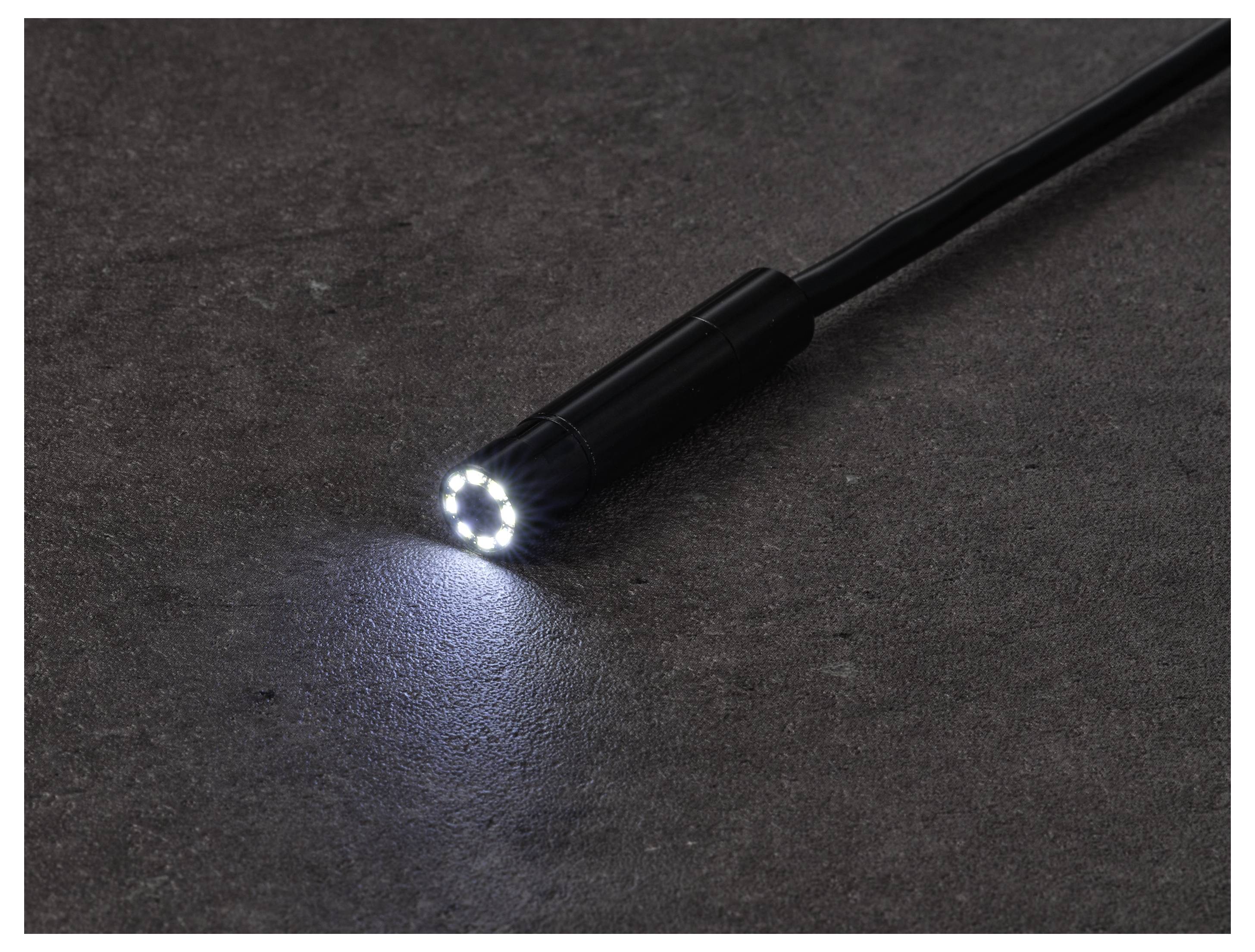 Een zwart zaklampje met de LED-straal aan, die een klein wit lichtcirceltje op een donker oppervlak schijnt.