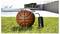 Een basketbal op gras naast een klein zwart apparaat, met een zwembad en een buitengang op de achtergrond.
