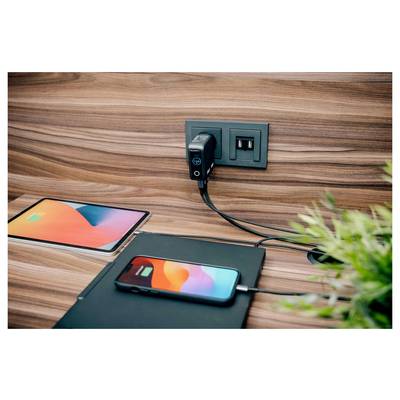 Een smartphone en tablet die op een houten bureau worden opgeladen, beide aangesloten op een wandcontactdoos met USB-poorten.