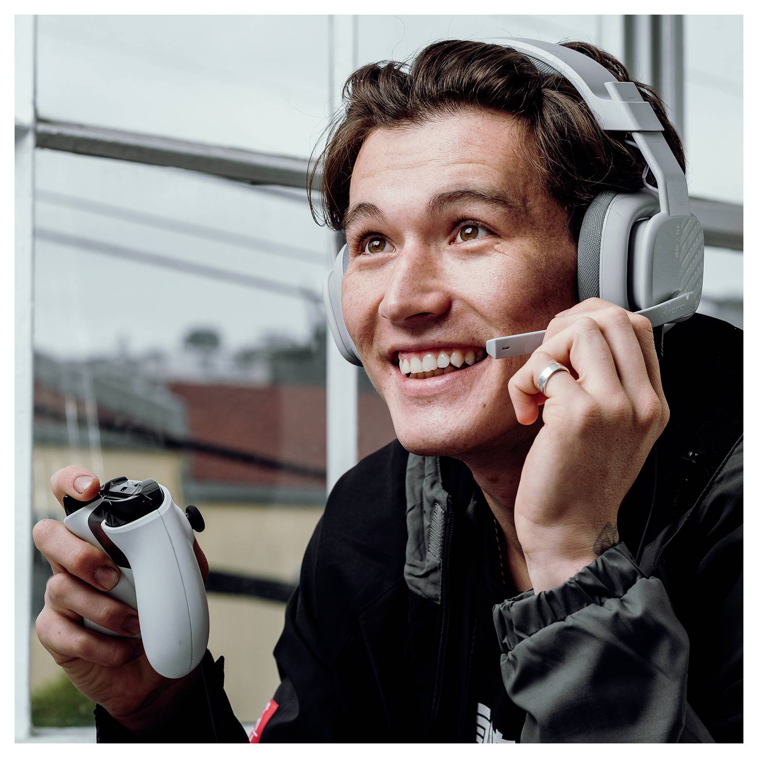 Glimlachende gamer die een headset draagt en een gamecontroller vasthoudt, terwijl hij tijdens het spelen in de microfoon spreekt.