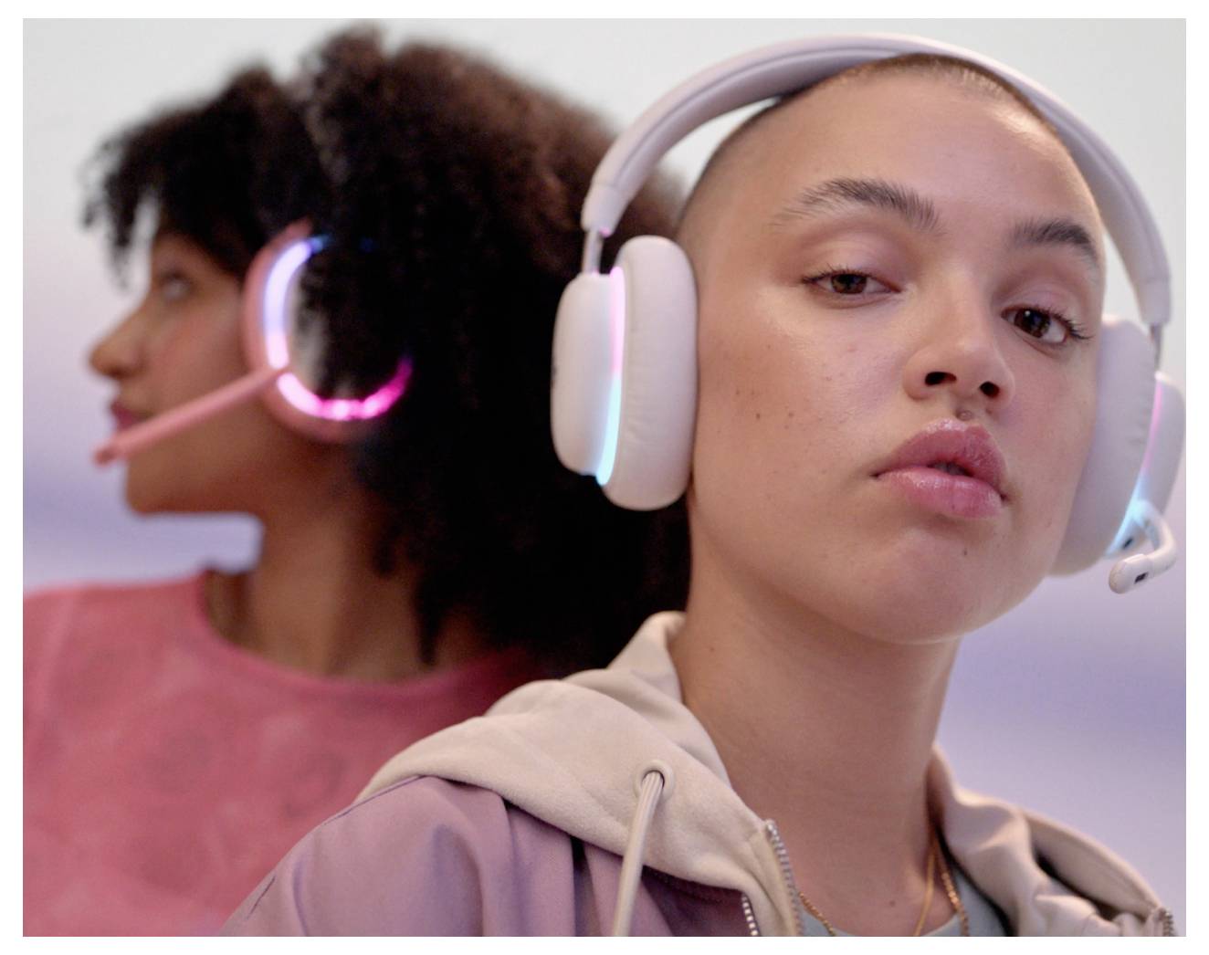 Twee vrouwen die gaming-headsets dragen, één op de voorgrond die naar de camera kijkt en één onscherp op de achtergrond die wegkijkt.