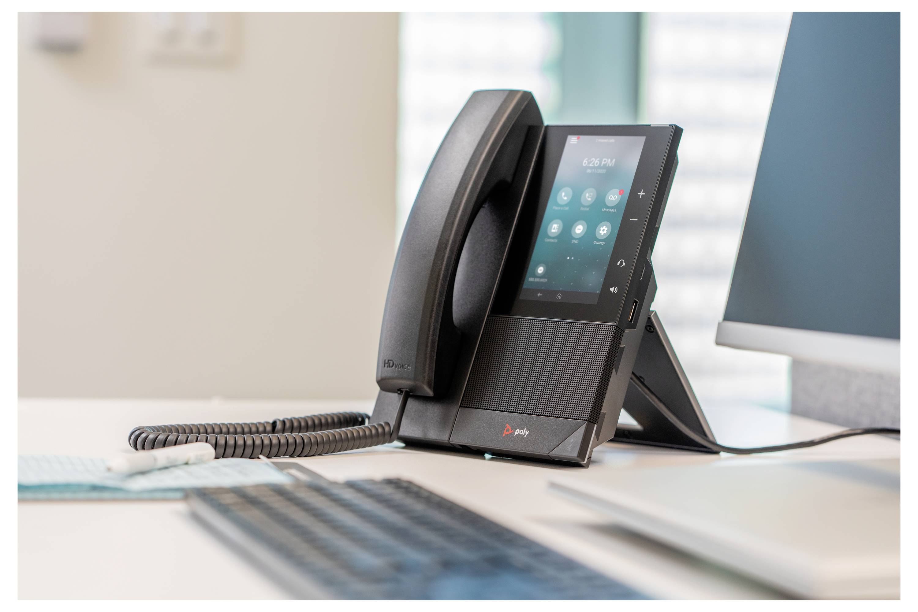 Een kantoor-bureautelefoon met aanraakscherm en handset op zijn standaard, met opgerolde kabel op de voorgrond.