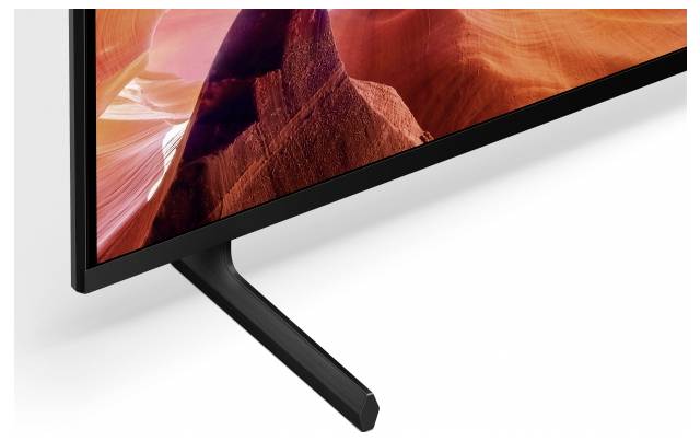 Close-up van een flatscreen-tv met een kleurrijke canyonafbeelding, met een zwart V-vormig standaard op een witte achtergrond.