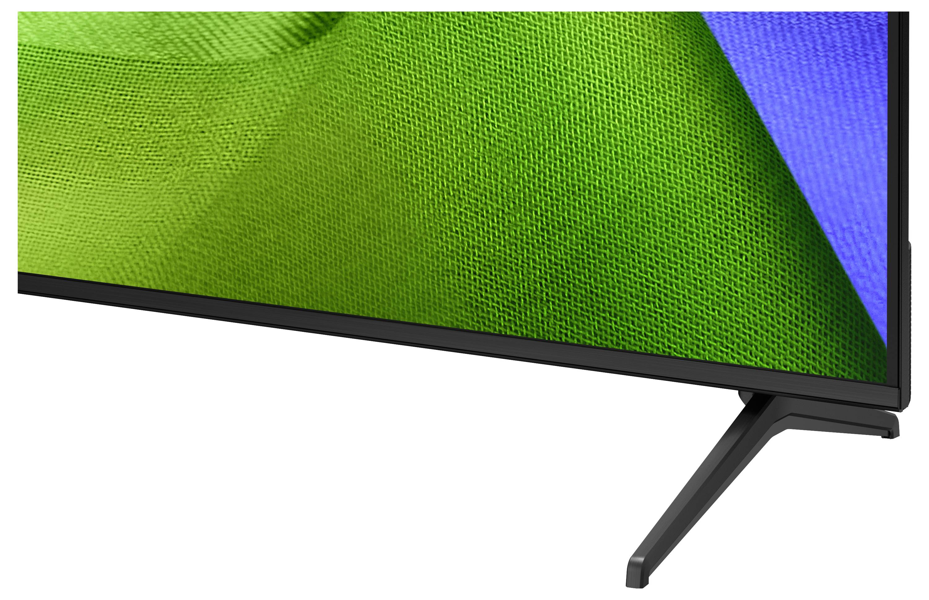 Close-up van een flatscreen-tv of monitor die een groen en blauw abstract display op een standaard toont.