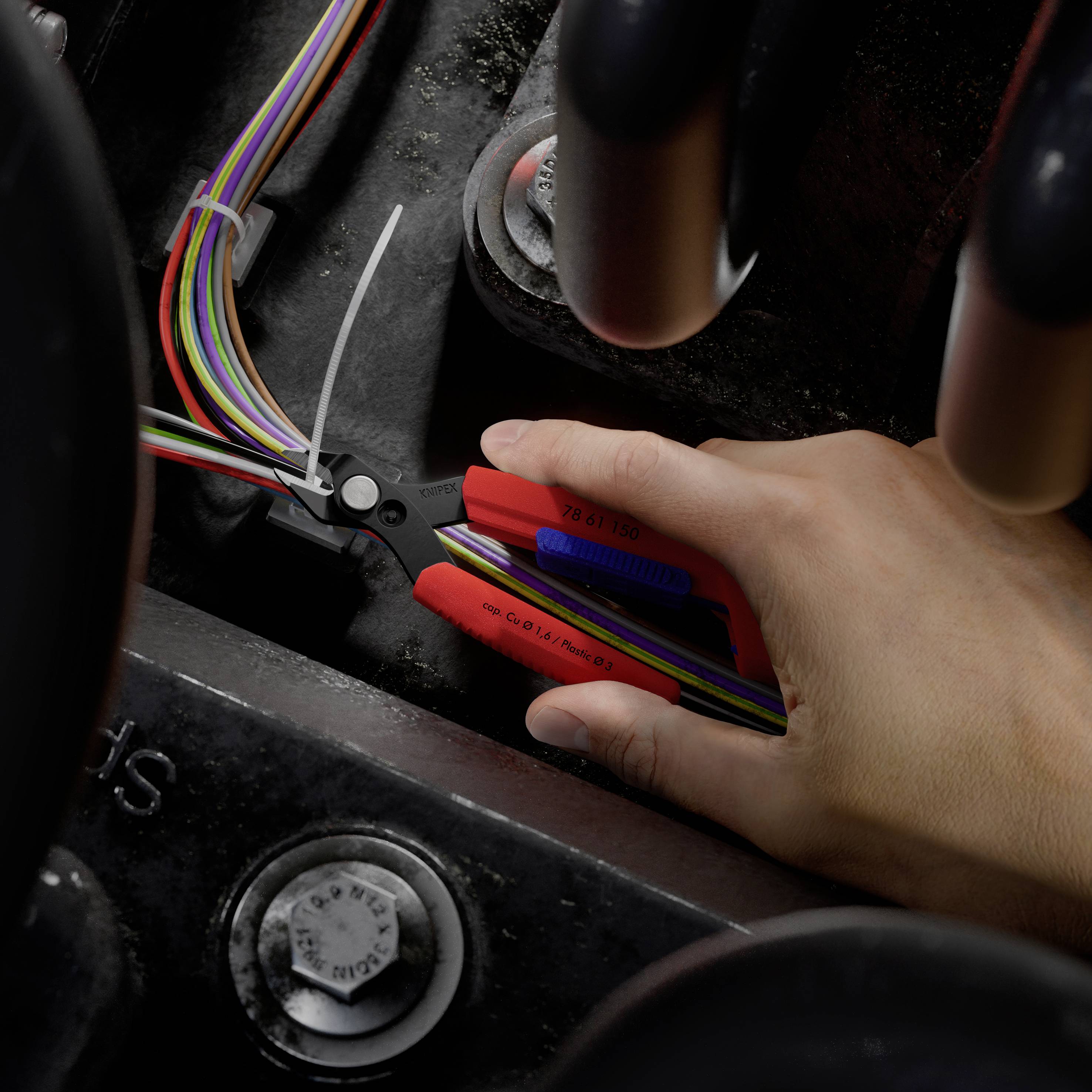 Hand met draadscharen die een bundel gekleurde elektrische draden in een voertuig- of machinecompartiment strippen.