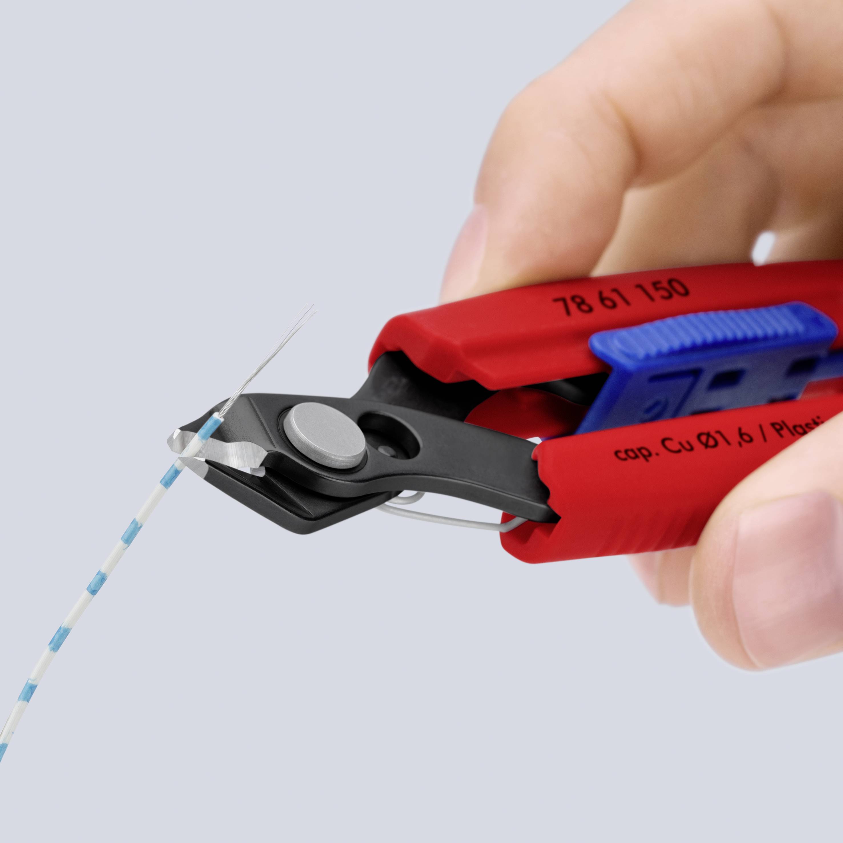 Close-up van een hand die draadknippers gebruikt om een dunne gestreepte draad tegen een effen achtergrond door te knippen.