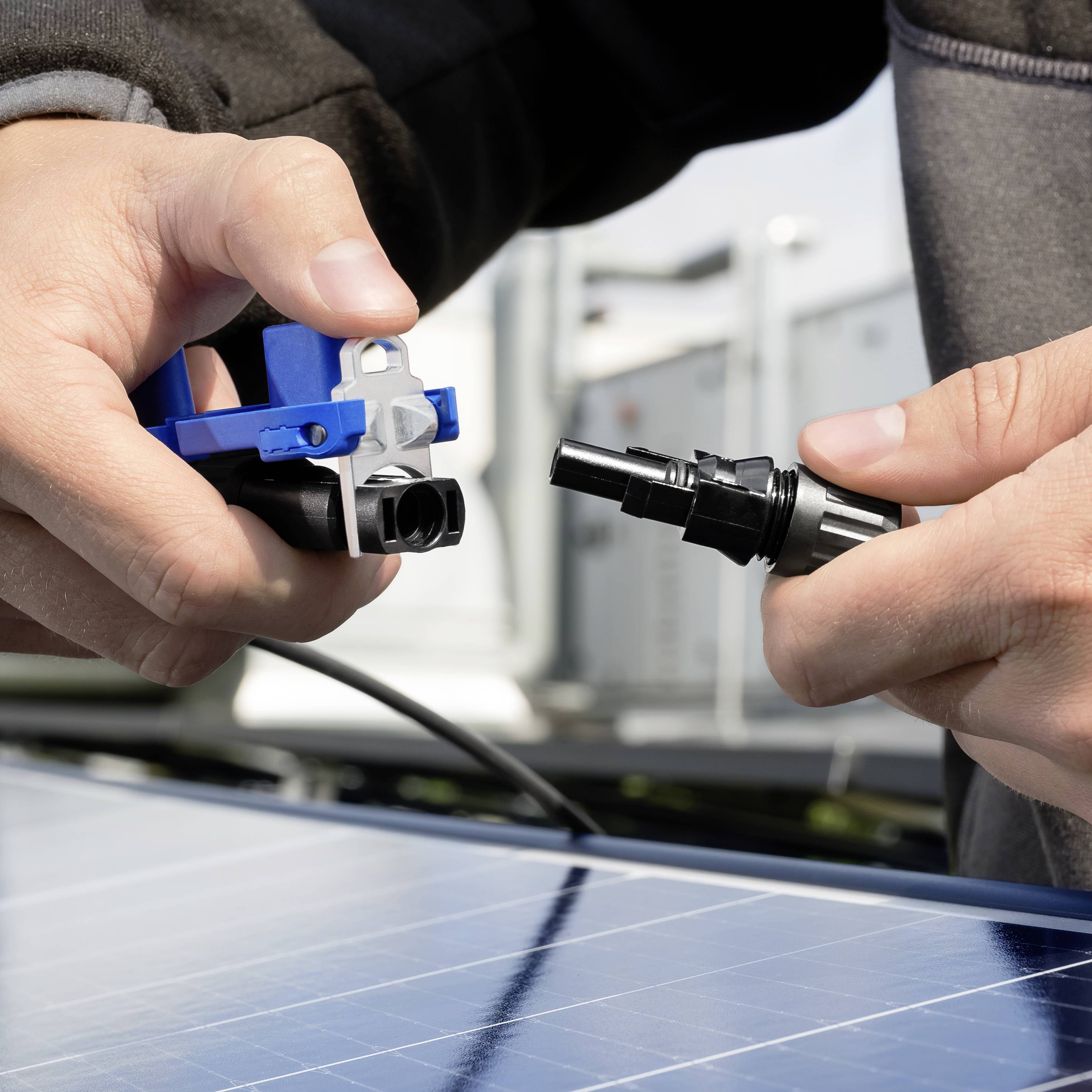 Schoon beeld van handen die een zonnepaneelkabel en -connector verbinden, wat duidt op installatie of onderhoud van fotovoltaïsche systemen.