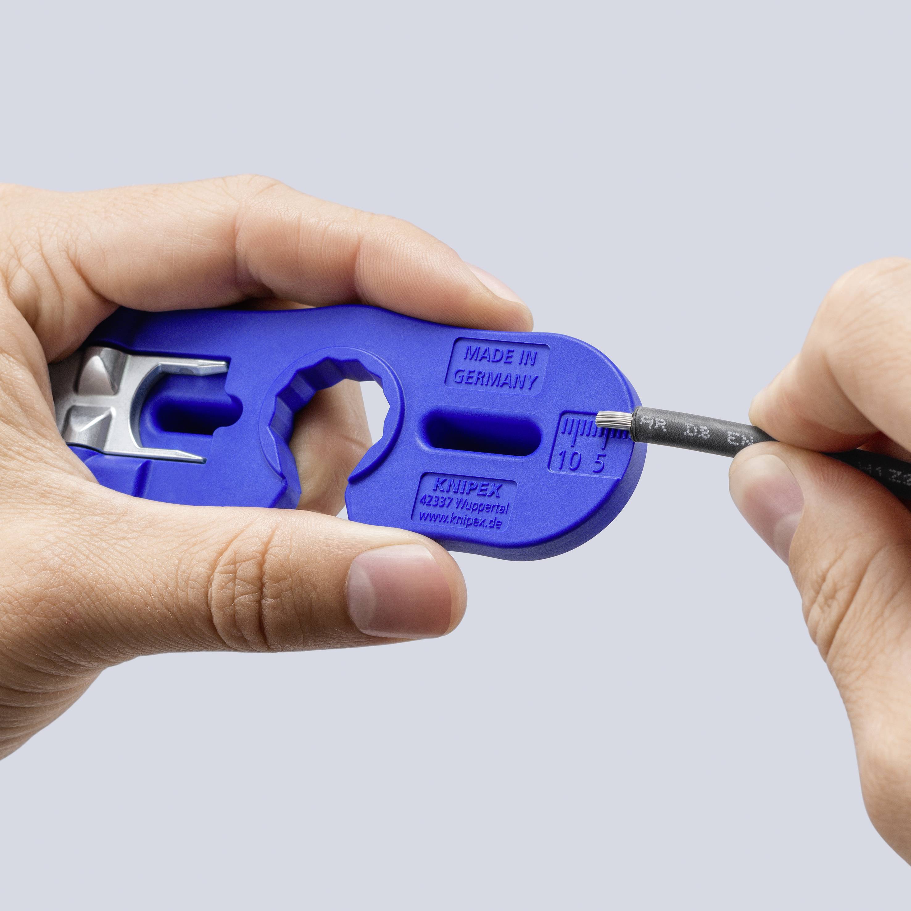 Handen gebruiken een blauwe KNIPEX-tool om een kabeldiameter tegen een ingebouwde meter te controleren die '10 5' en 'Made in Germany' markeert.