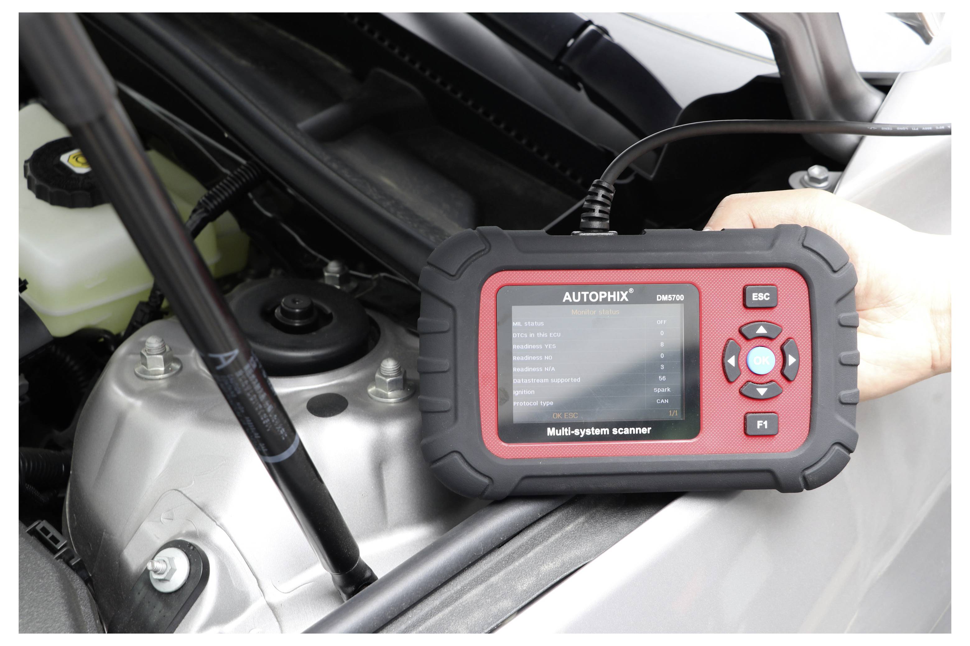 Handheld AUTOPHIX multisysteemscanner die in een motorruimte van een auto wordt gebruikt voor voertuigdiagnose.