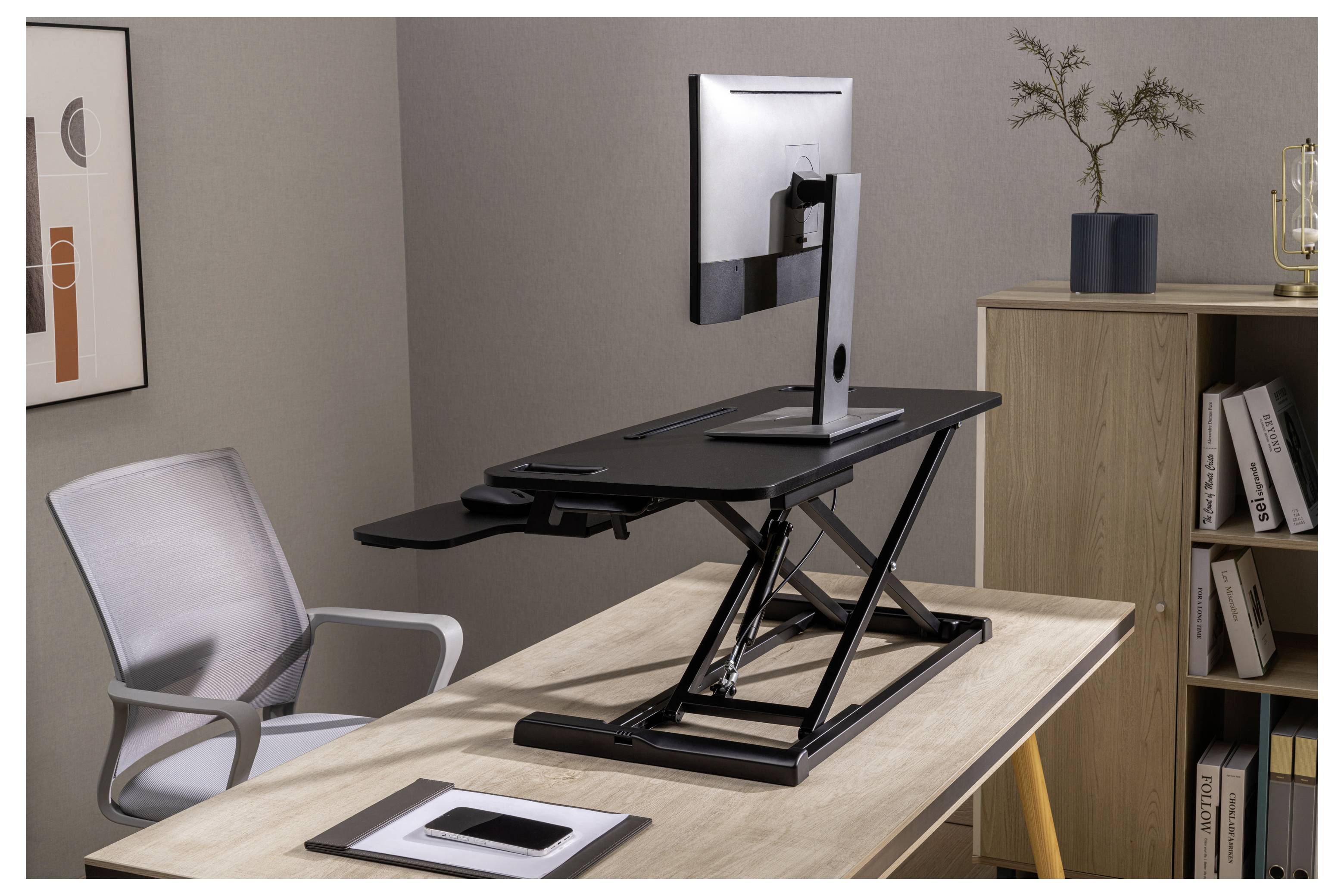 Verstelbare staande bureauomzetter op een houten bureau, met een monitor en toetsenbord in een thuiskantoor.