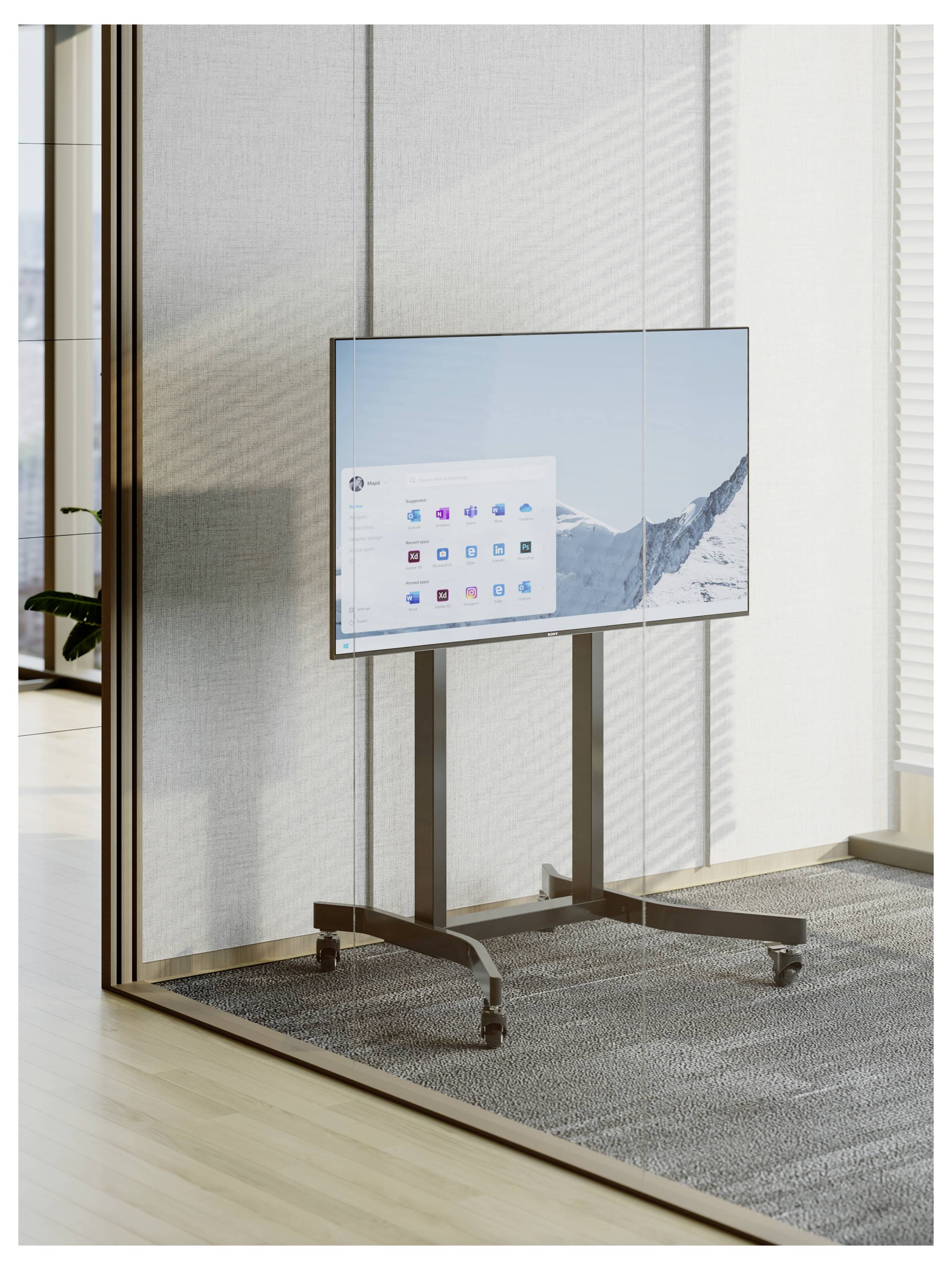Flatscreen-scherm op een verrijdbare standaard in een modern kantoor, met een computerhomescherm met app-pictogrammen over een achtergrond van sneeuw bedekte bergen.