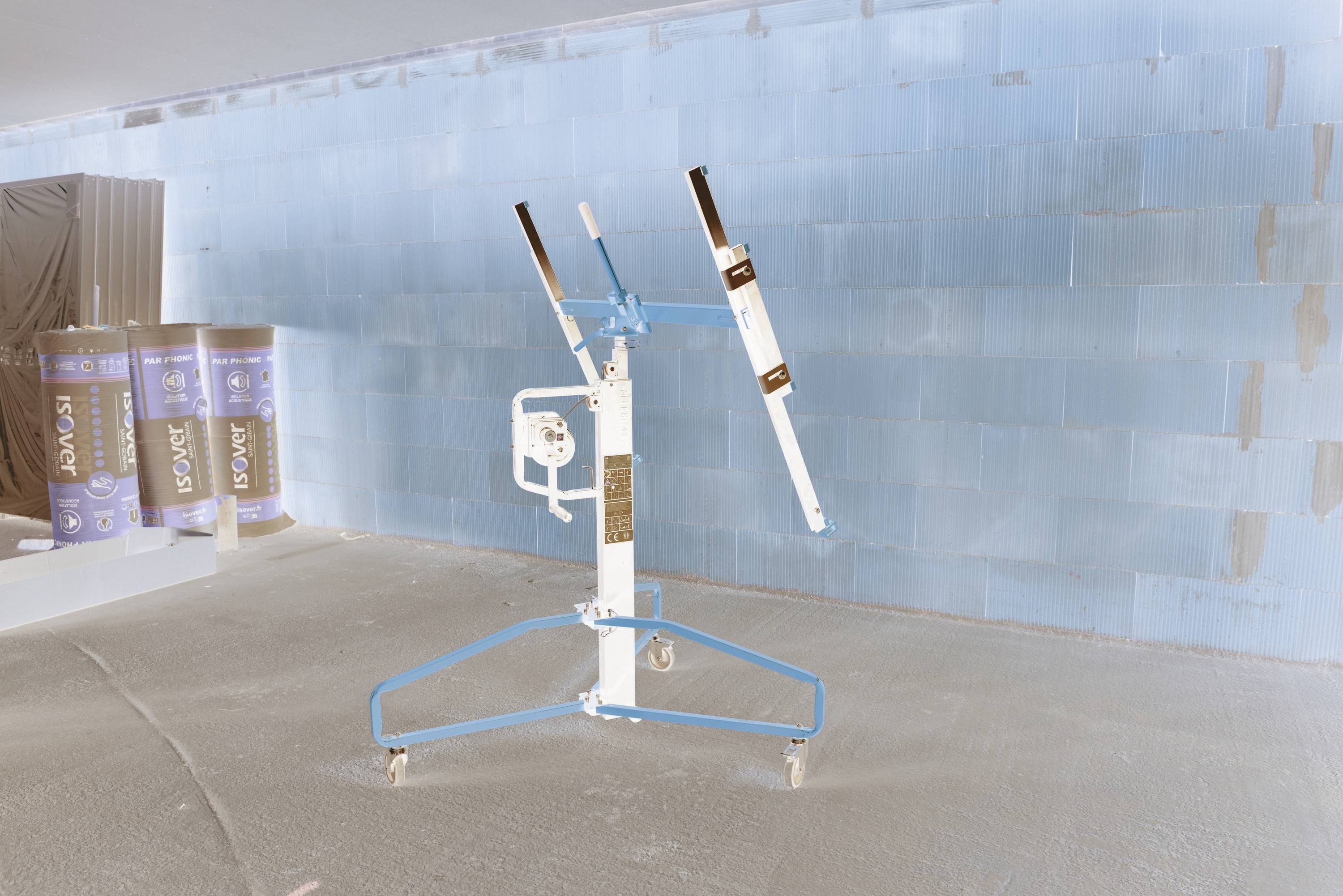 Een wielbouwkraan met blauwe steunbalken en een verstelbare witte giek staat op een betonnen vloer in een magazijnachtige ruimte.