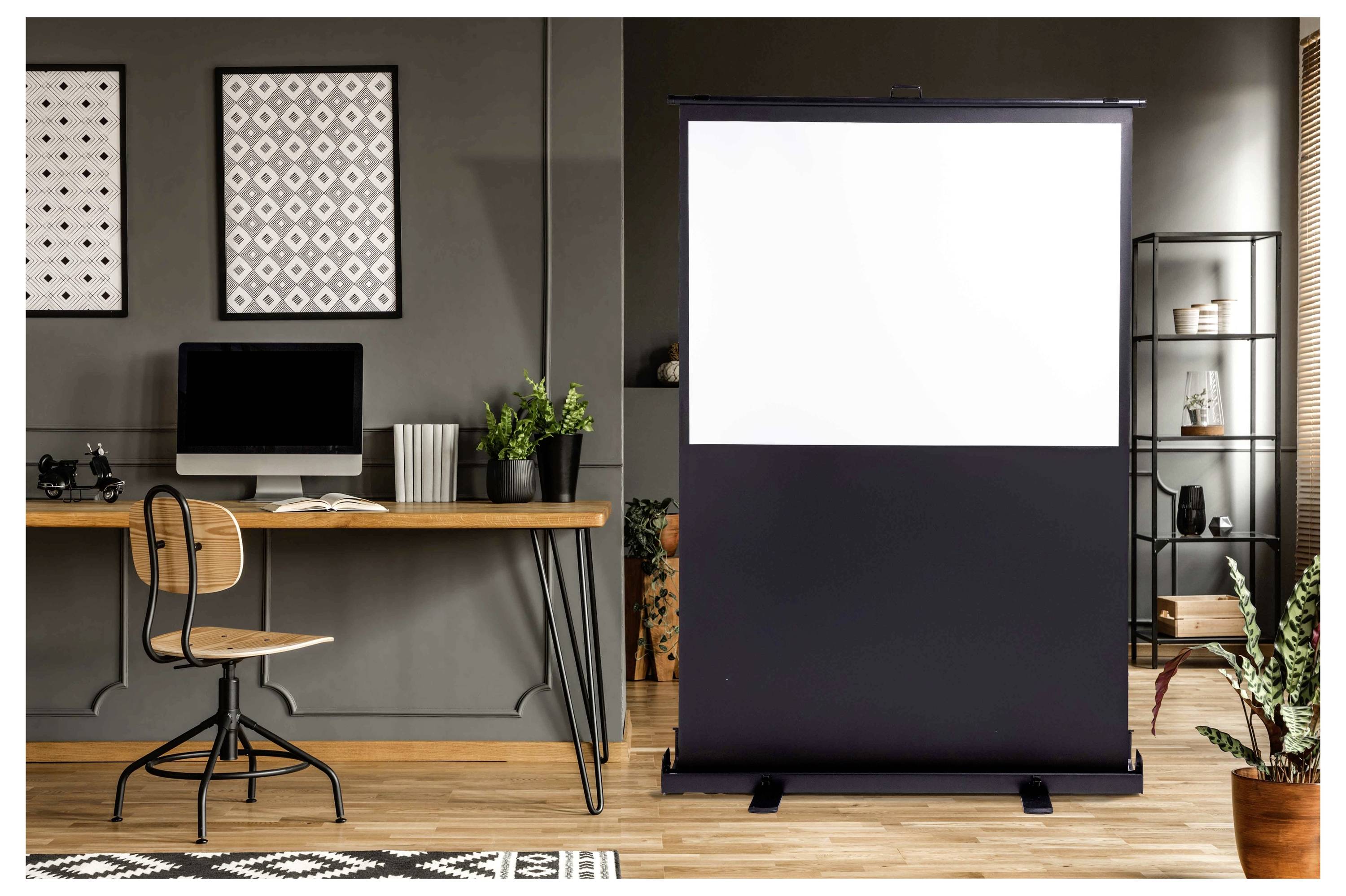 Thuiswerkplek met een leeg uitrolscherm voor de projector naast een bureau, stoel, computer en decoratie, wat suggereert dat dit een presentatie- of werkruimte is.