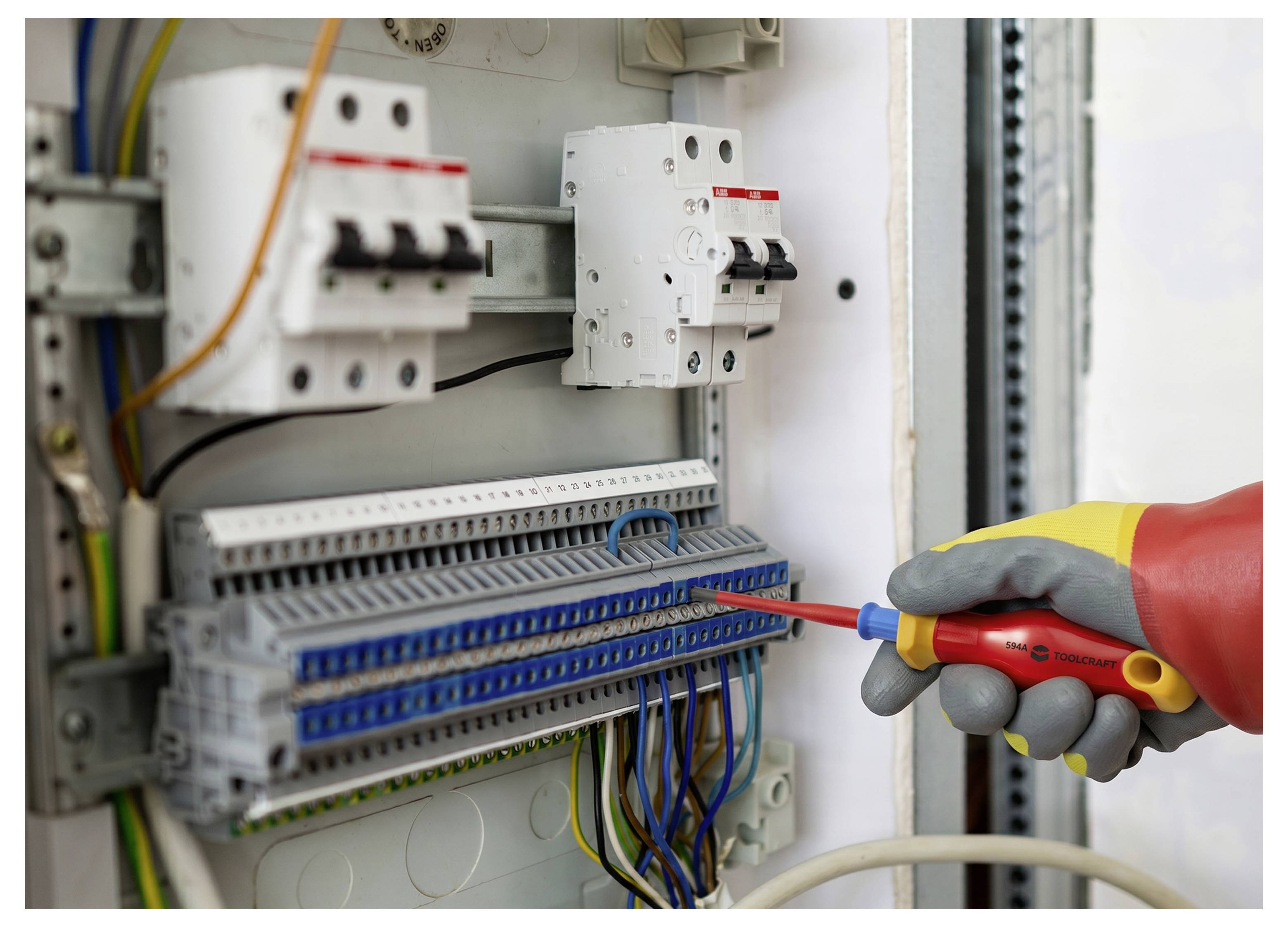 Gehandschoende hand gebruikt een geïsoleerde schroevendraaier om bedrading in een elektrisch bedieningspaneel met automaten en aansluitblokken af te stellen.