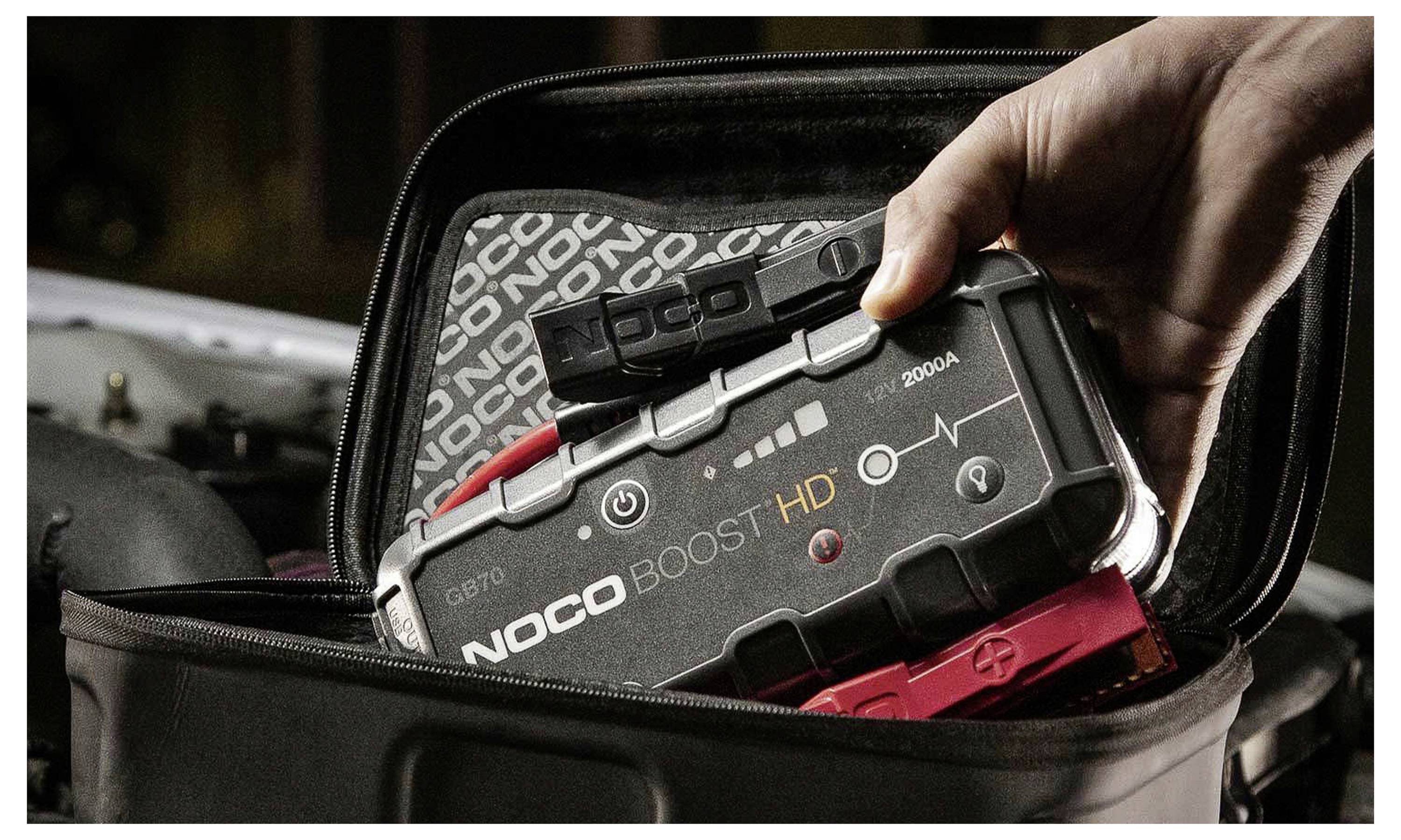 Hand plaatst een NOCO Boost HD draagbare jumpstarter in een open draagtas.