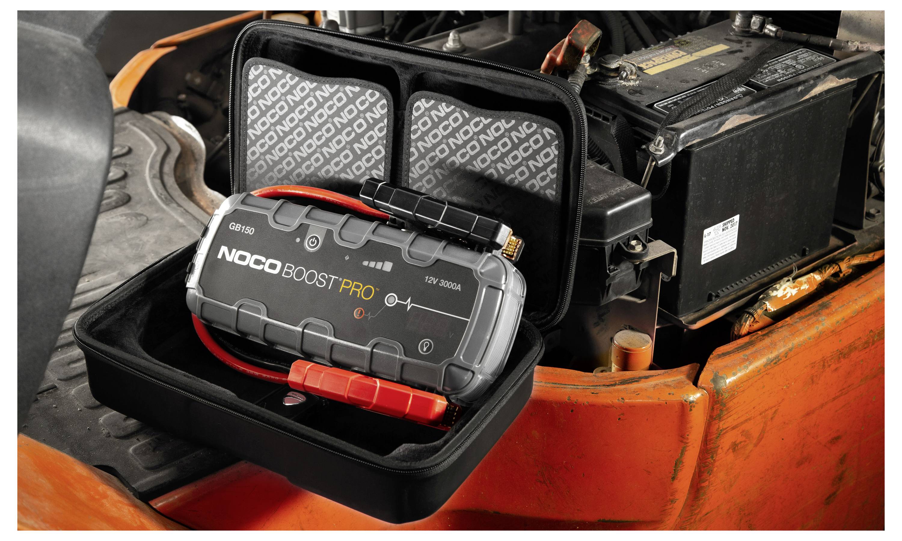 Draagbare NOCO Boost Pro jumpstarter in een open koffer naast een autoaccu, gebruikt voor noodstart van voertuigen.
