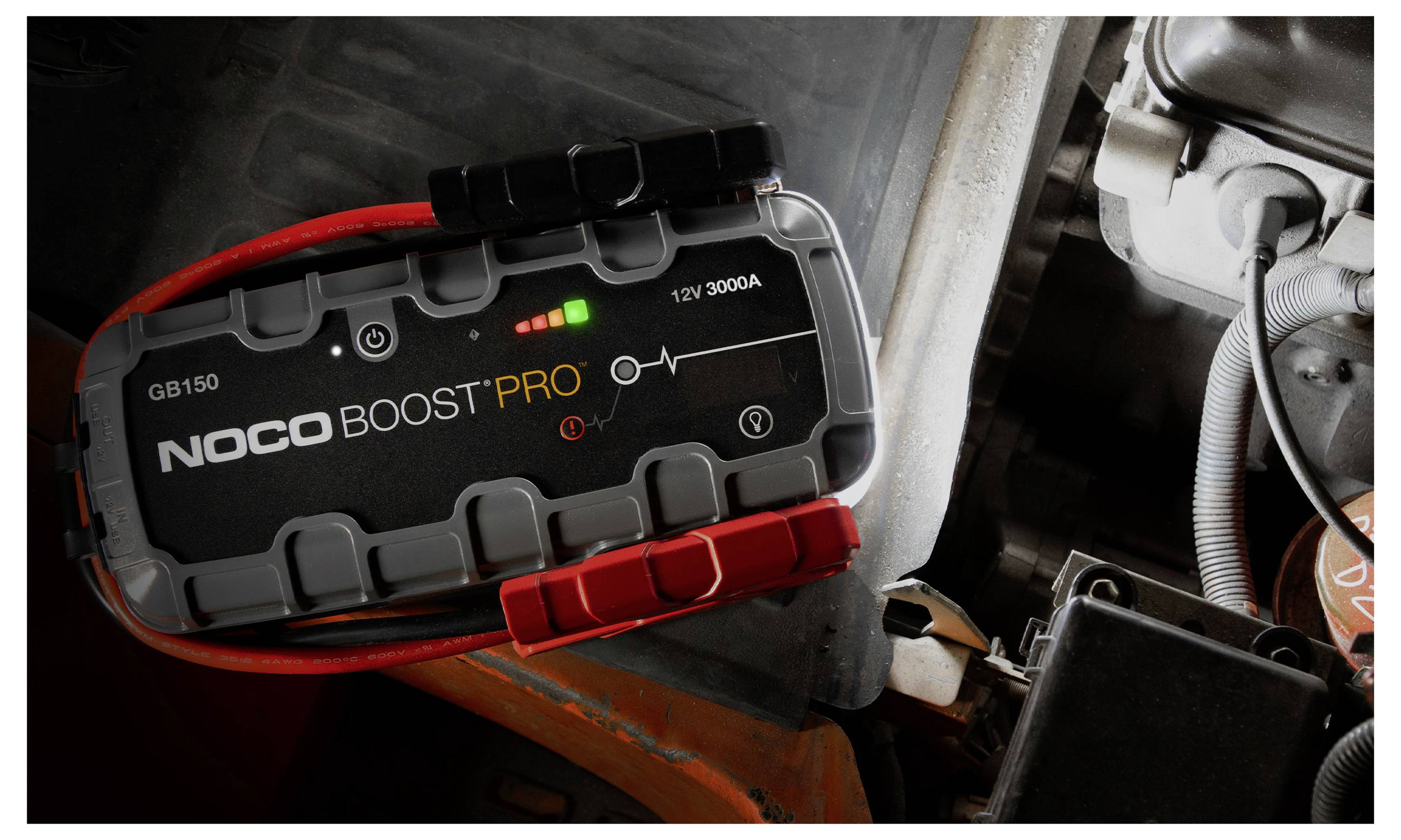 NOCO Boost Pro draagbare autostarthulp aangesloten in een motorruimte, met indicatorlampjes die de stroomstatus weergeven.
