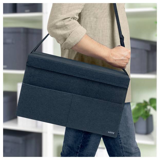 Persoon met een donkerblauwe schoudertas voor laptops, weergegeven van torso tot dij binnenshuis.