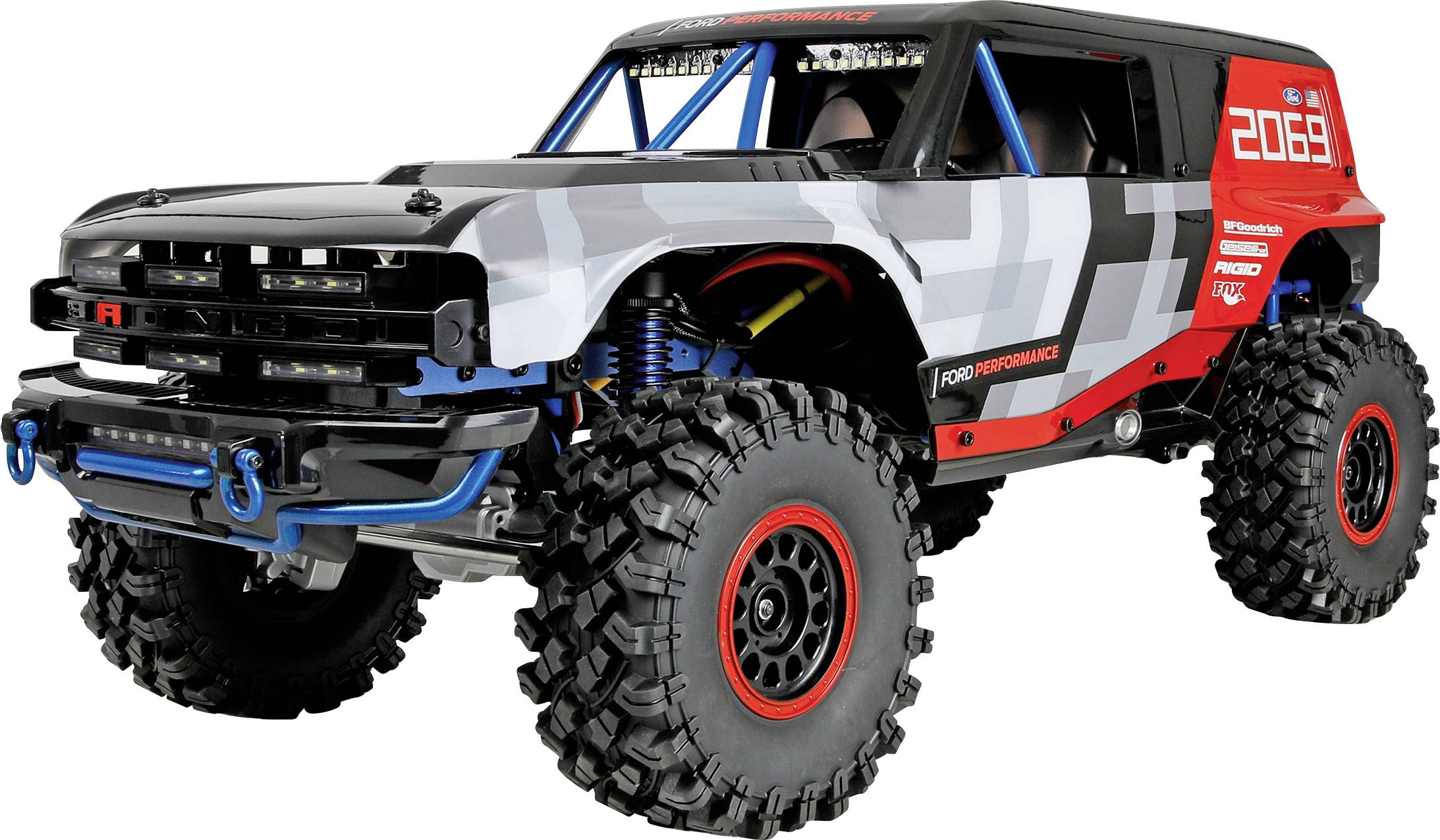 Zwart, grijs en rood off-road RC-vrachtwagen met oversized knobbelige banden, rolkooi en voorste sleepophangen, weergegeven op een witte achtergrond.